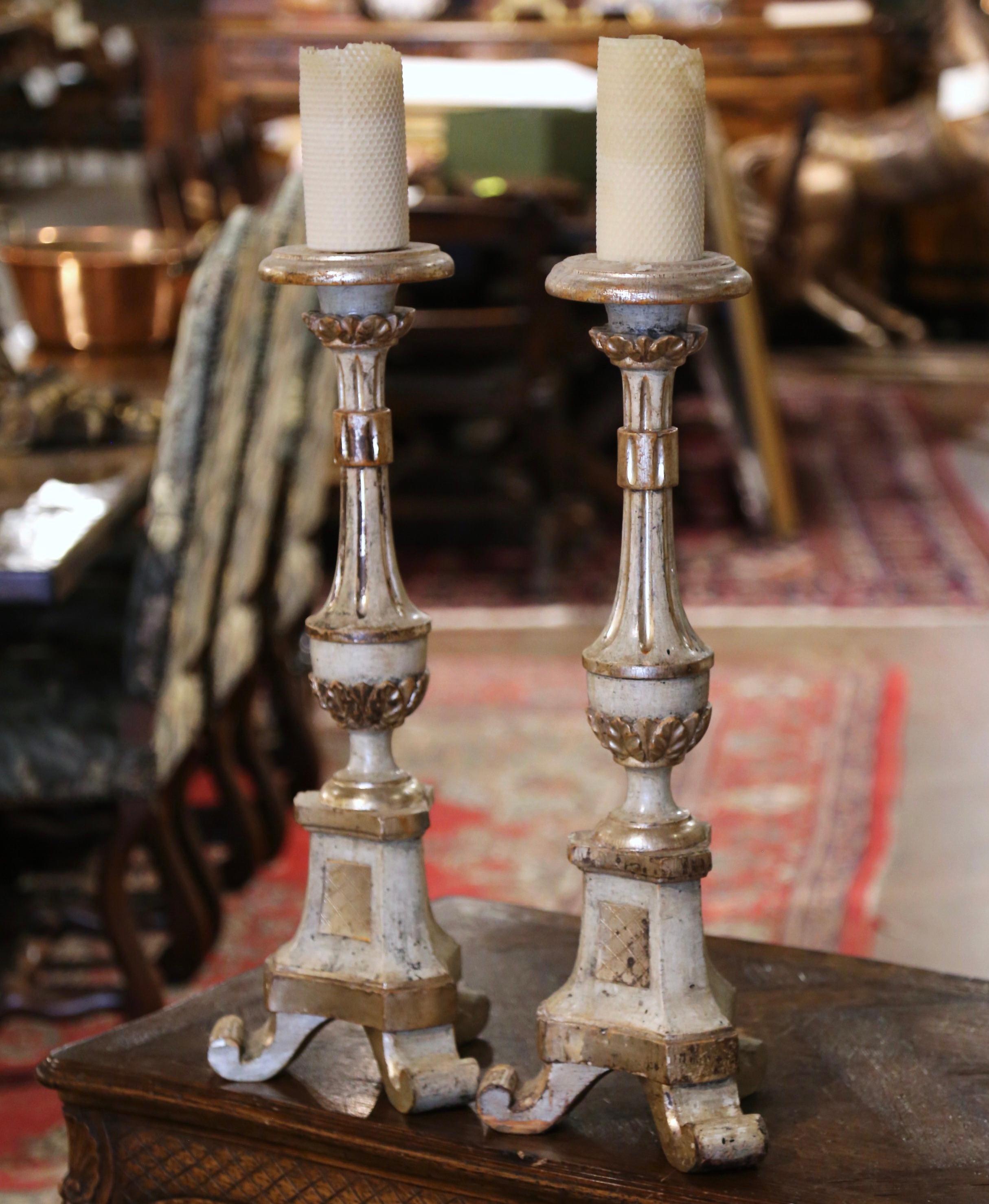 Add an air of drama and elegance to your home with this elegant pair of antique candlesticks. Crafted in Italy circa 1880, each candle holder stands on a tripod base ending with scrolled feet; the tall decorative fluted stem is embellished with hand