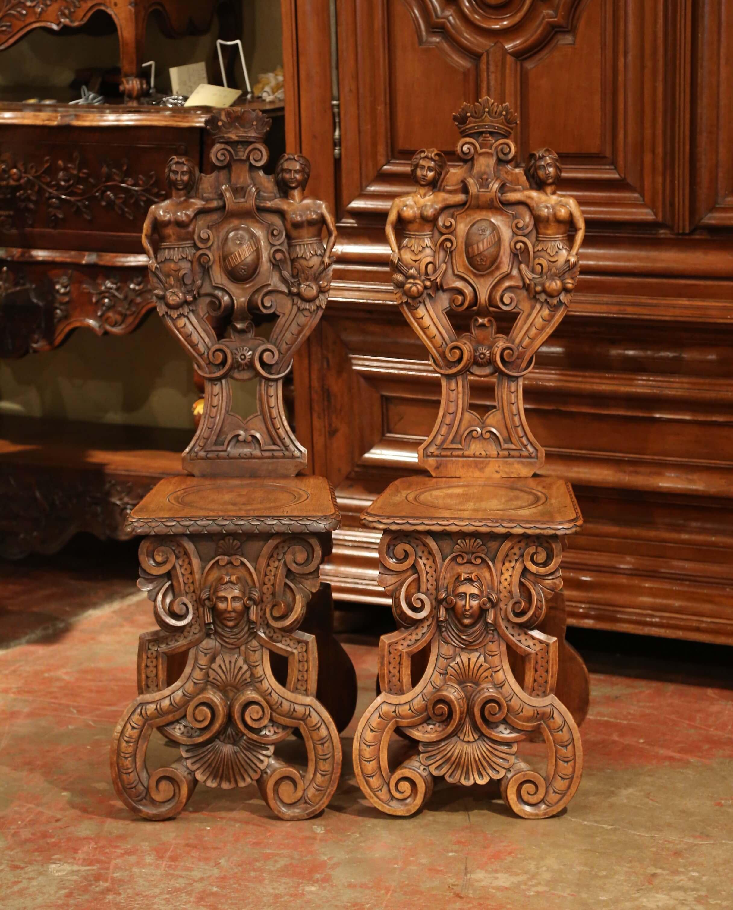 Decorate a hallway with this well carved pair of antique Sgabello chairs. Crafted of walnut in Italy circa 1860, each Renaissance chair stands on curved legs, decorated in the center with a female face figure, and embellished with shell and foliage