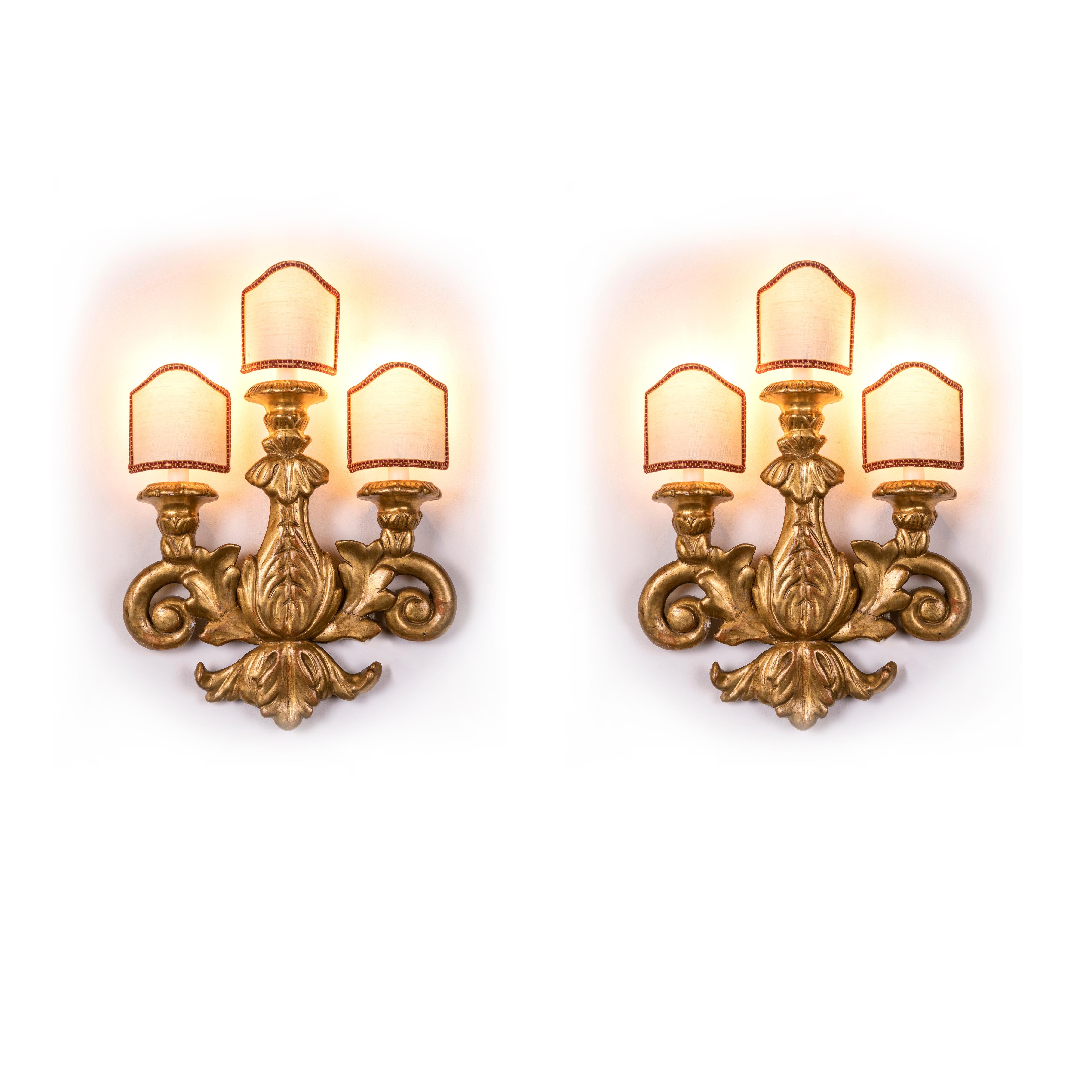 A pair of antique carved with vegetal patterns and gilded wooden wall-lights, Italian three-light sconces dating back to early 19th century. 
They came from a private house of Milan and we presume they were originally part of a larger liturgical