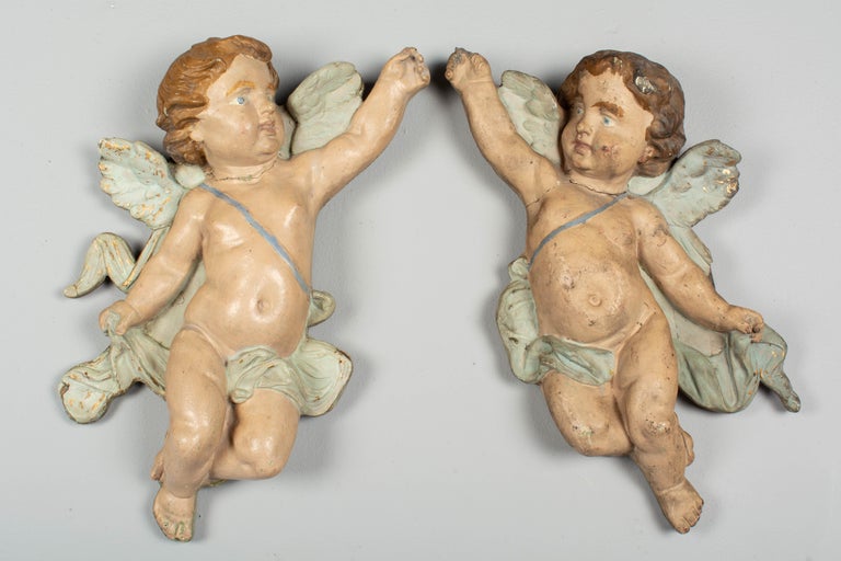A pair of 19th century Italian polychrome painted winged putti wall sculptures made of terracotta mounted to pine planks. In good condition with nice patina and traces of original gilt painted details. These were likely altar decorations from a