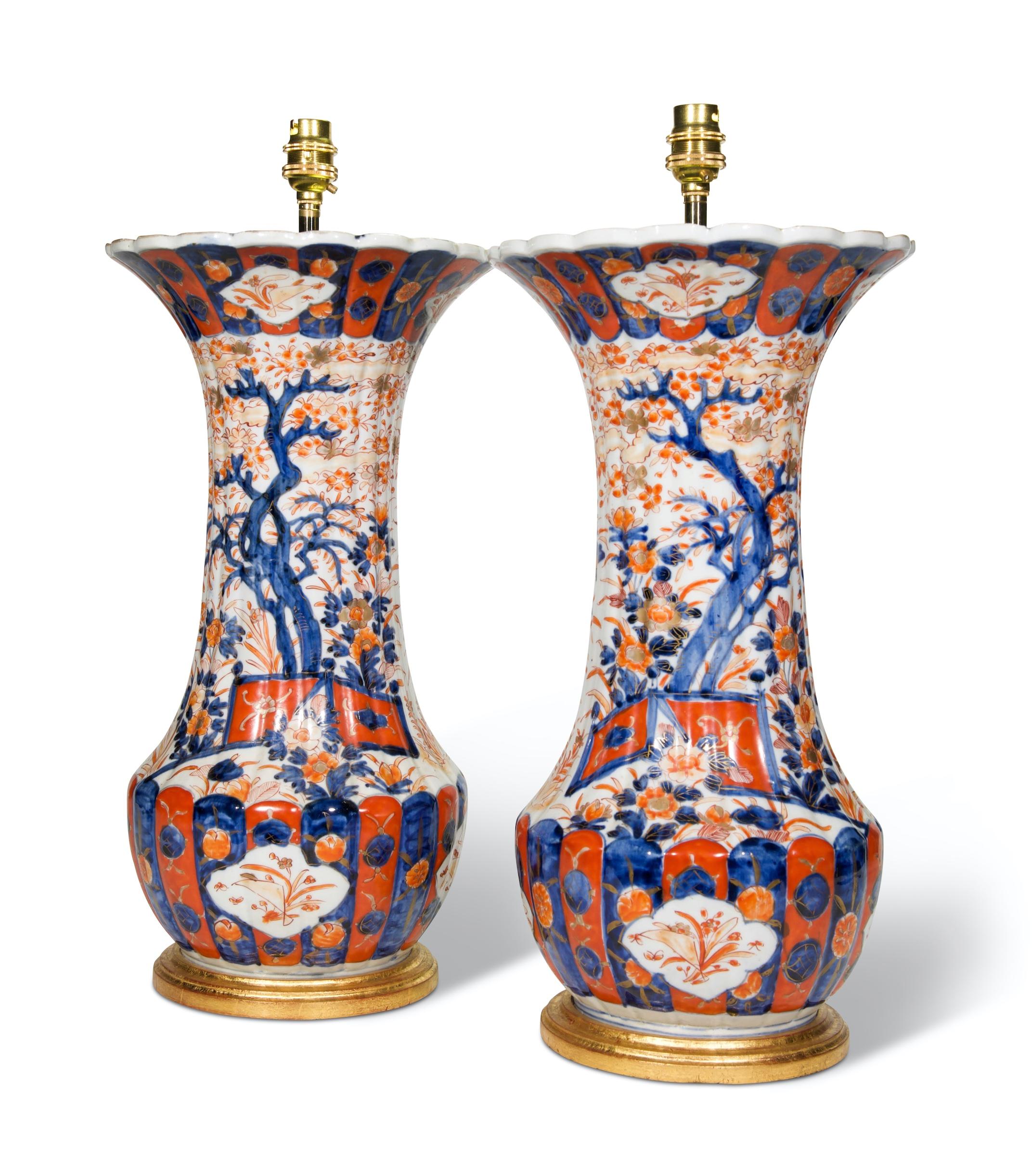 A fine pair of Chinese Imari late 19th century baluster vases, decorated with floral and foliate garden scenes in the typical Imari palette of iron reds and blues with gold highlights on a white background, with ribbed bodies and flared necks. Now