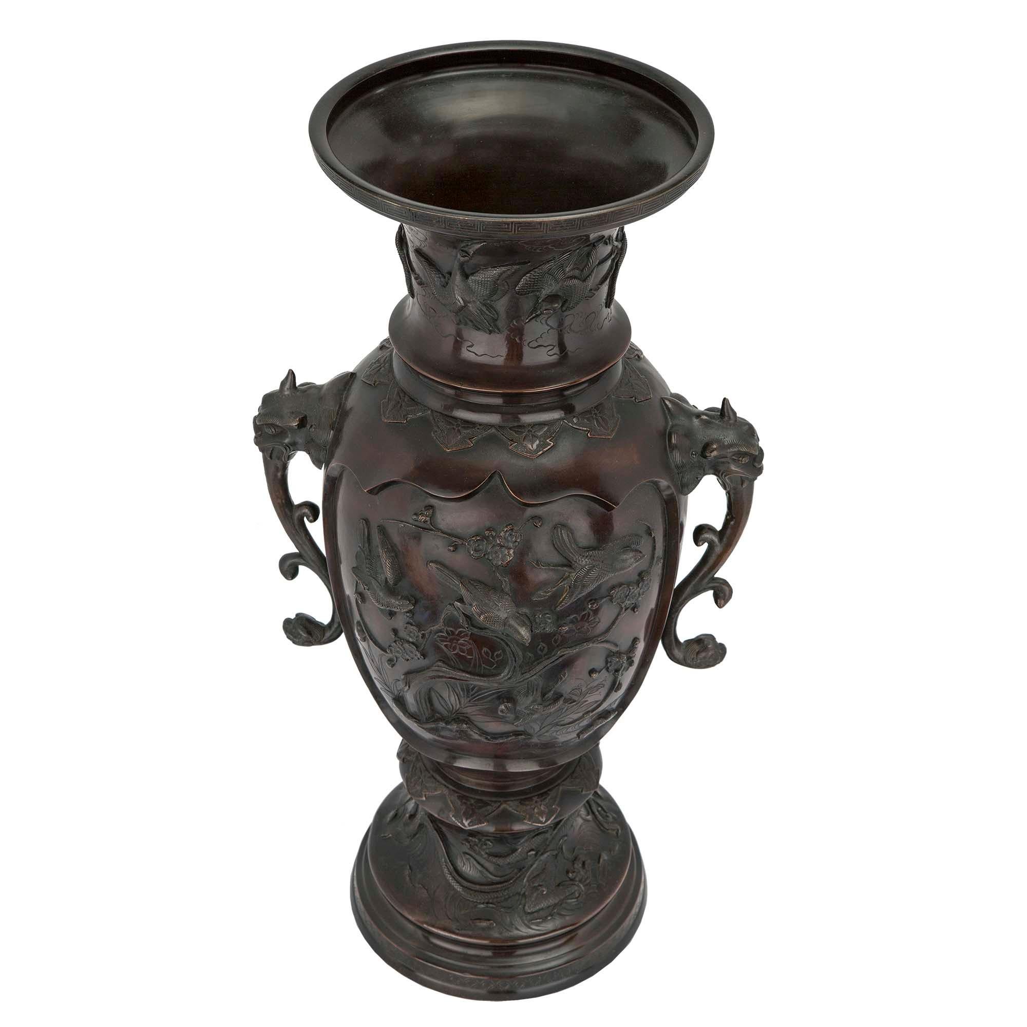 A very handsome and large scale 19th century Japanese Meiji Period patinated bronze urns. Each urn is raised on a circular mottled base. The urns are decorated throughout with scenes of birds and foliate. At each side is a foo dog mask with scrolled