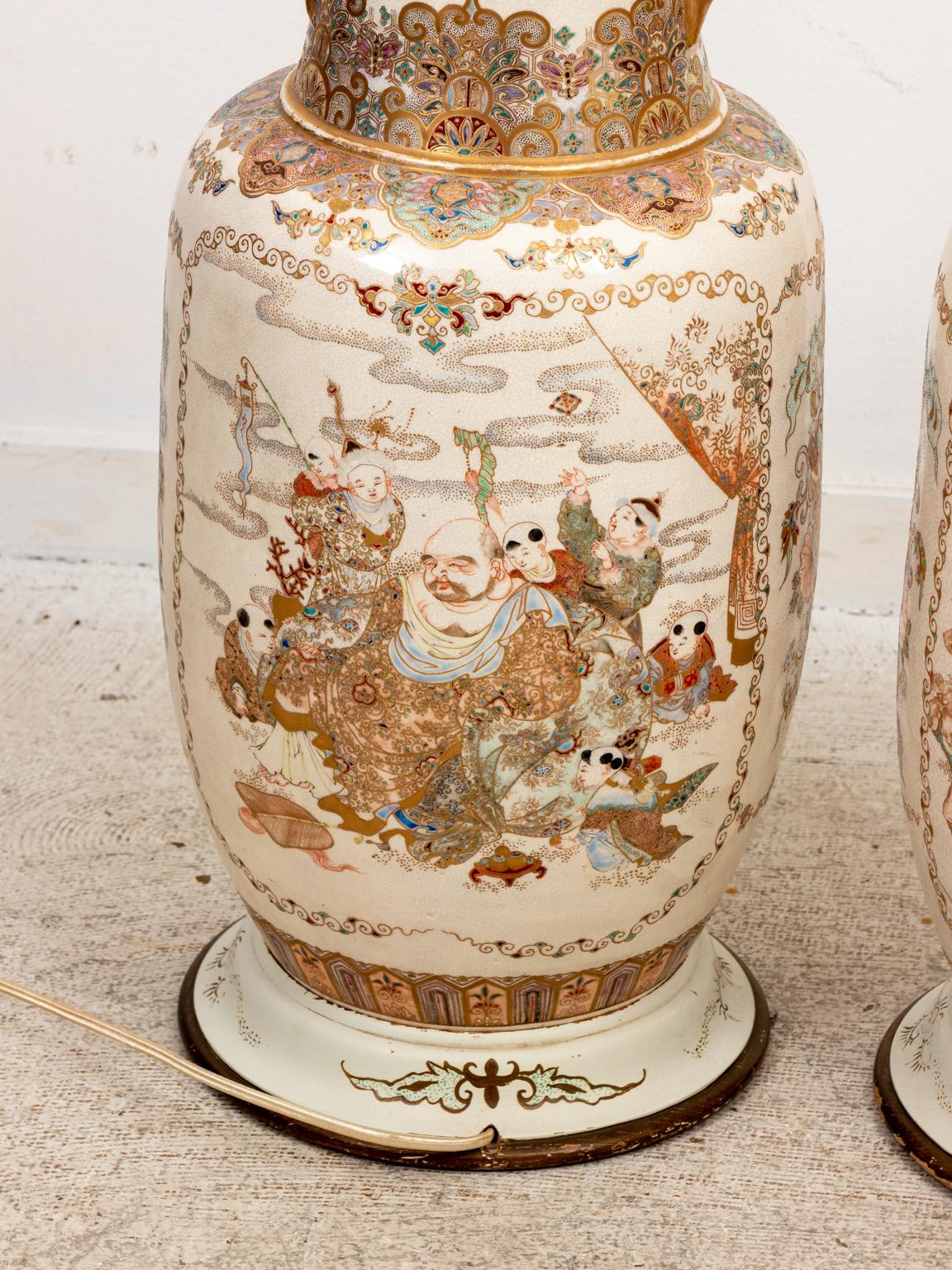 Circa 19th century pair of painted ceramic Japanese Satsuma vase table lamps with ornately detailed panels on the body, neck, and base. Some of the illustrations include stylized Japanese figures, cranes, and geometric trim. Shades not included.