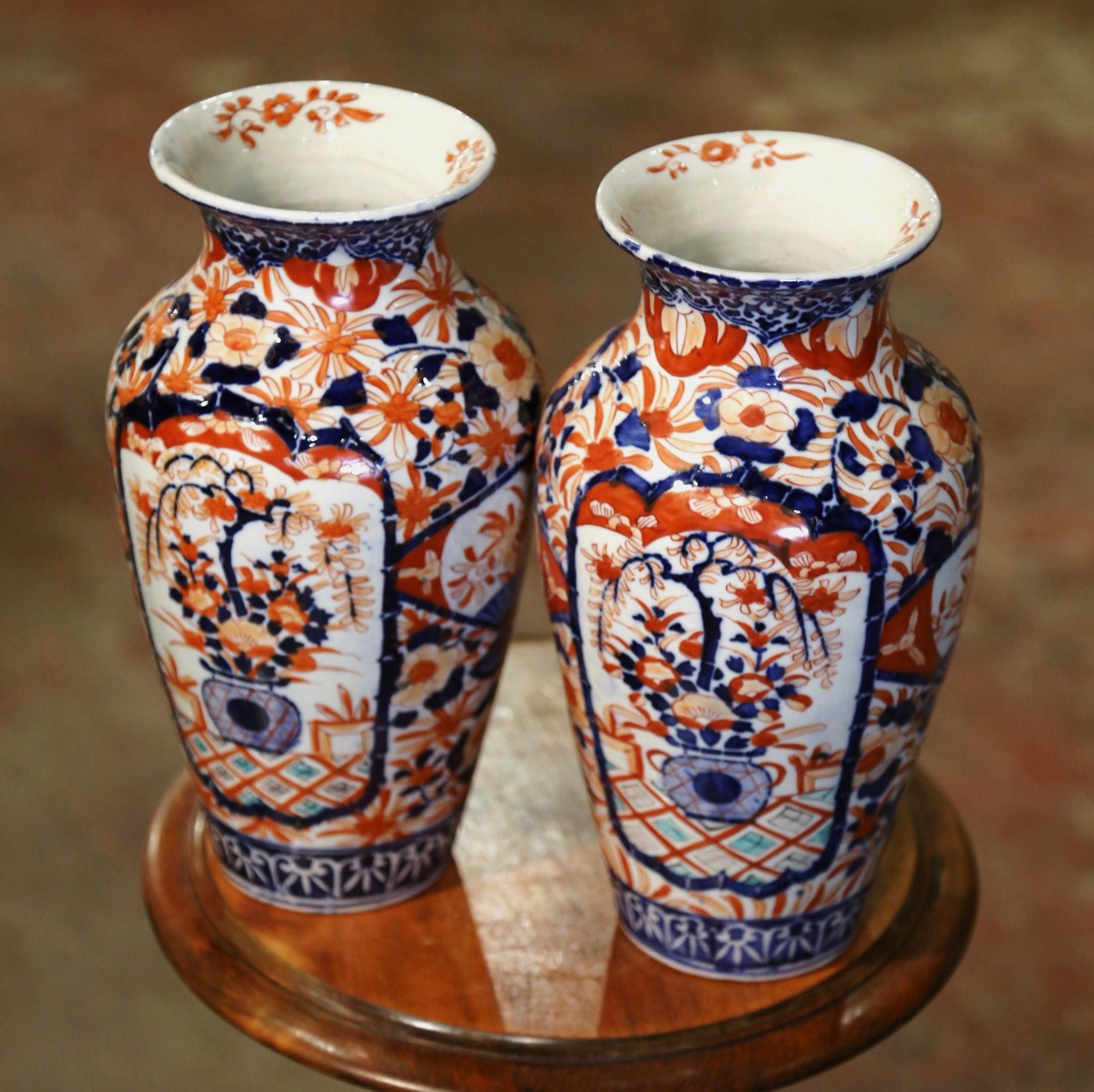 Decorate a mantel or a buffet with this colorful pair of antique Imari vases. Crafted in Japan, circa 1880 and round in shape, the ceramic vessels are hand painted with floral and plant motifs in the traditional rust, white and blue Imari palette.
