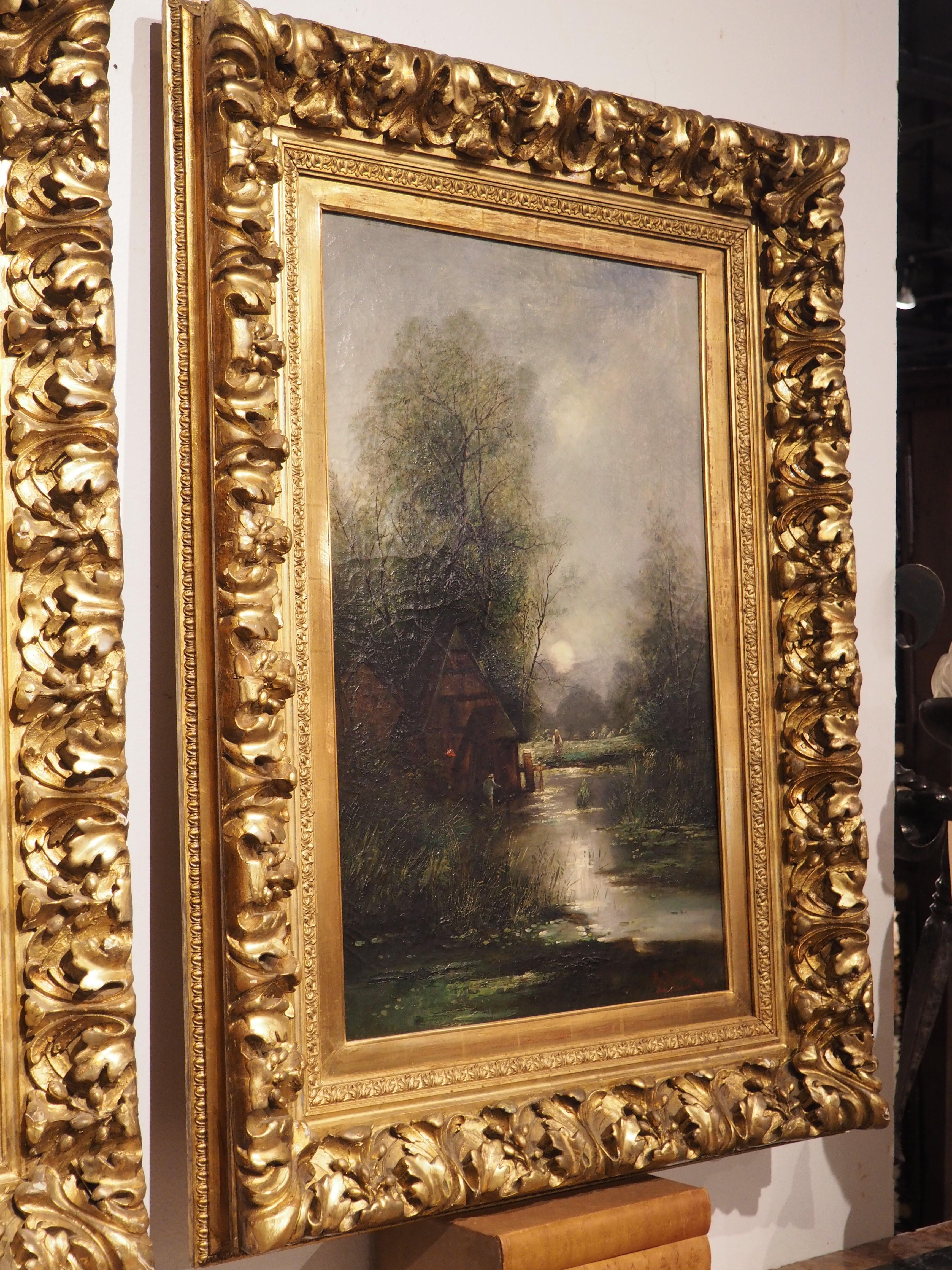 A one-of-a-kind set of signed German paintings, these vertically oriented landscapes are elegantly ensconced within identical large foliate giltwood frames. The first offering transports viewers to a tranquil countryside scene. In this pastoral