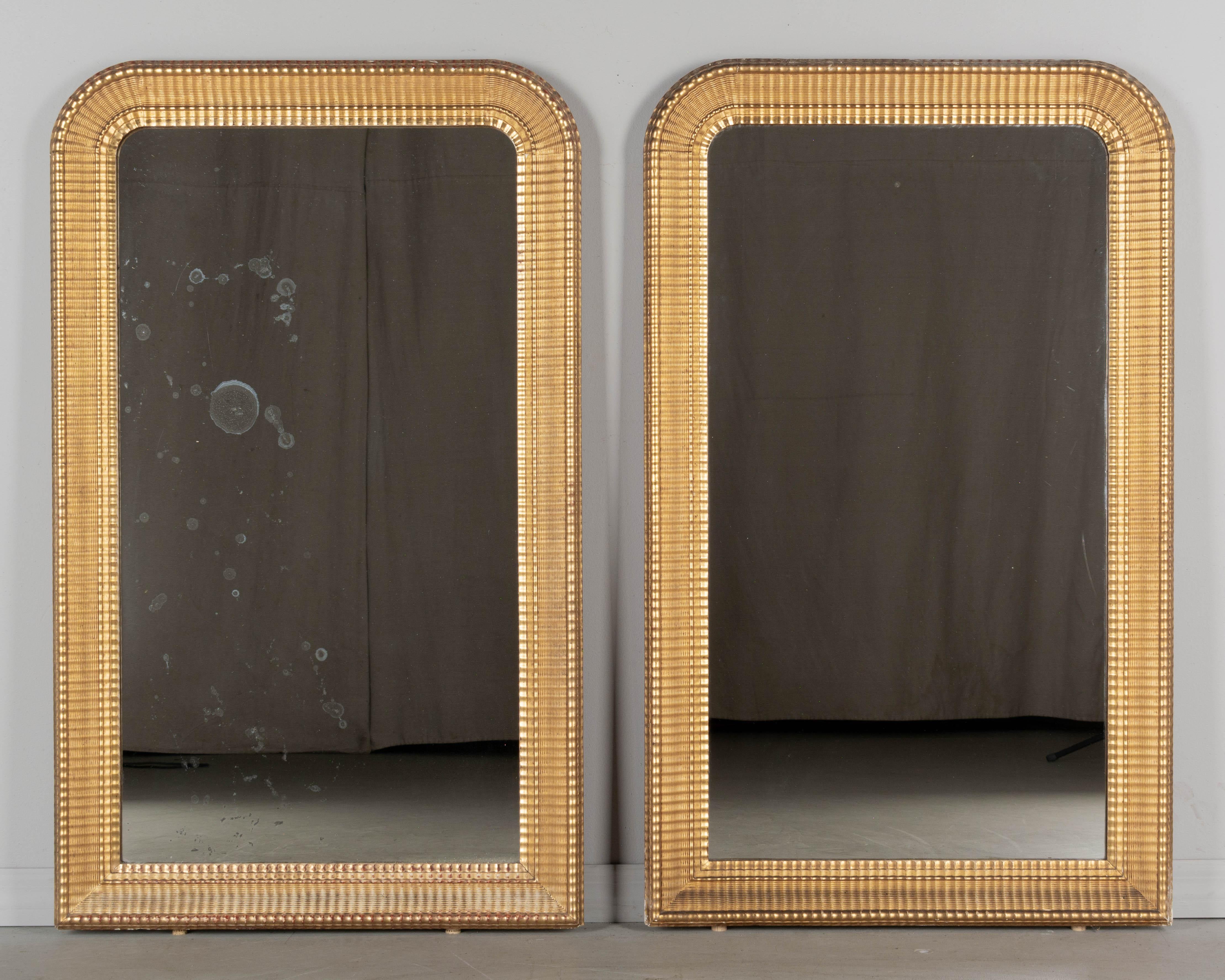 A pair of 19th century French Louis Philippe style giltwood mirrors with curved top, 3.5 inch wide ribbed frame with warm gilt finish. Original mirror with old silvering, one with some spotting. Minor loss to gilt. Circa 1880-1900. 
Dimensions: