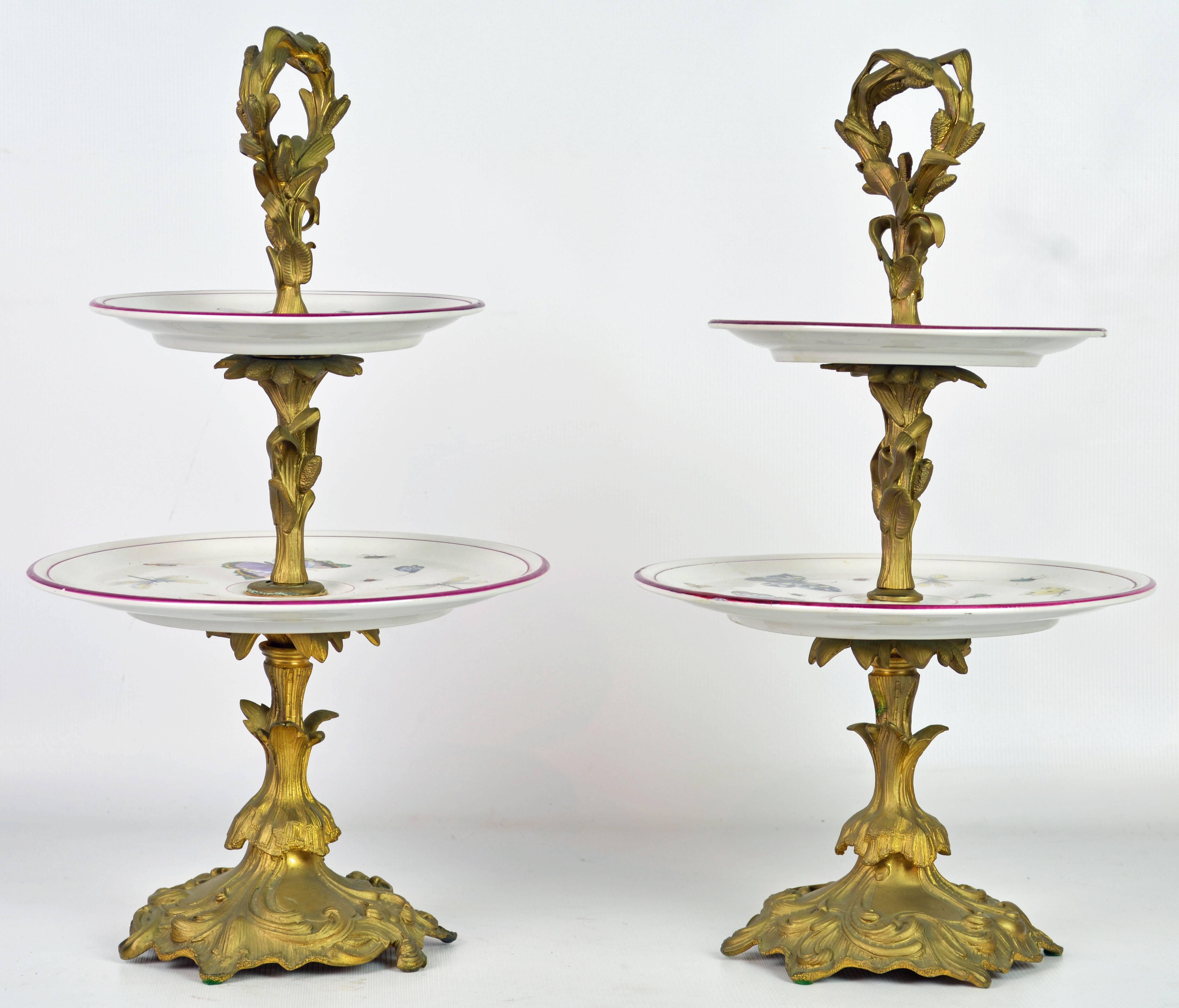 A lovely and unusual pair of almost 18 inches tall rococo or Louis XV style two-tier gilt bronze dessert stands with Old Paris porcelain tiers decorated with butterflies, dragonflies and insects.