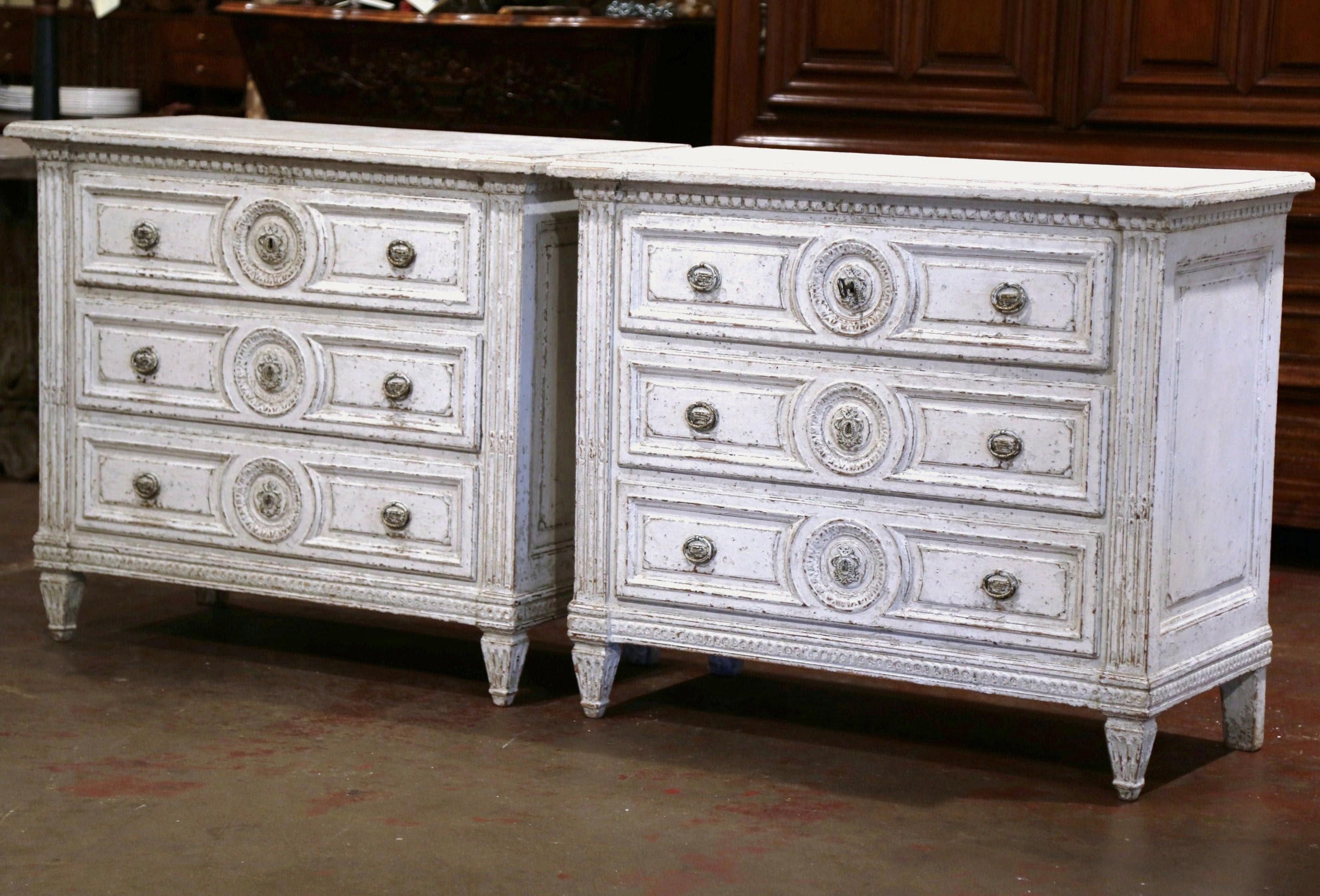 Use this elegant pair of antique painted chests of drawers on either side of a mantel, on in an entry way. Crafted in France, circa 1860, each commode sits on tapered and fluted feet, and features detailed carved decor including a center round