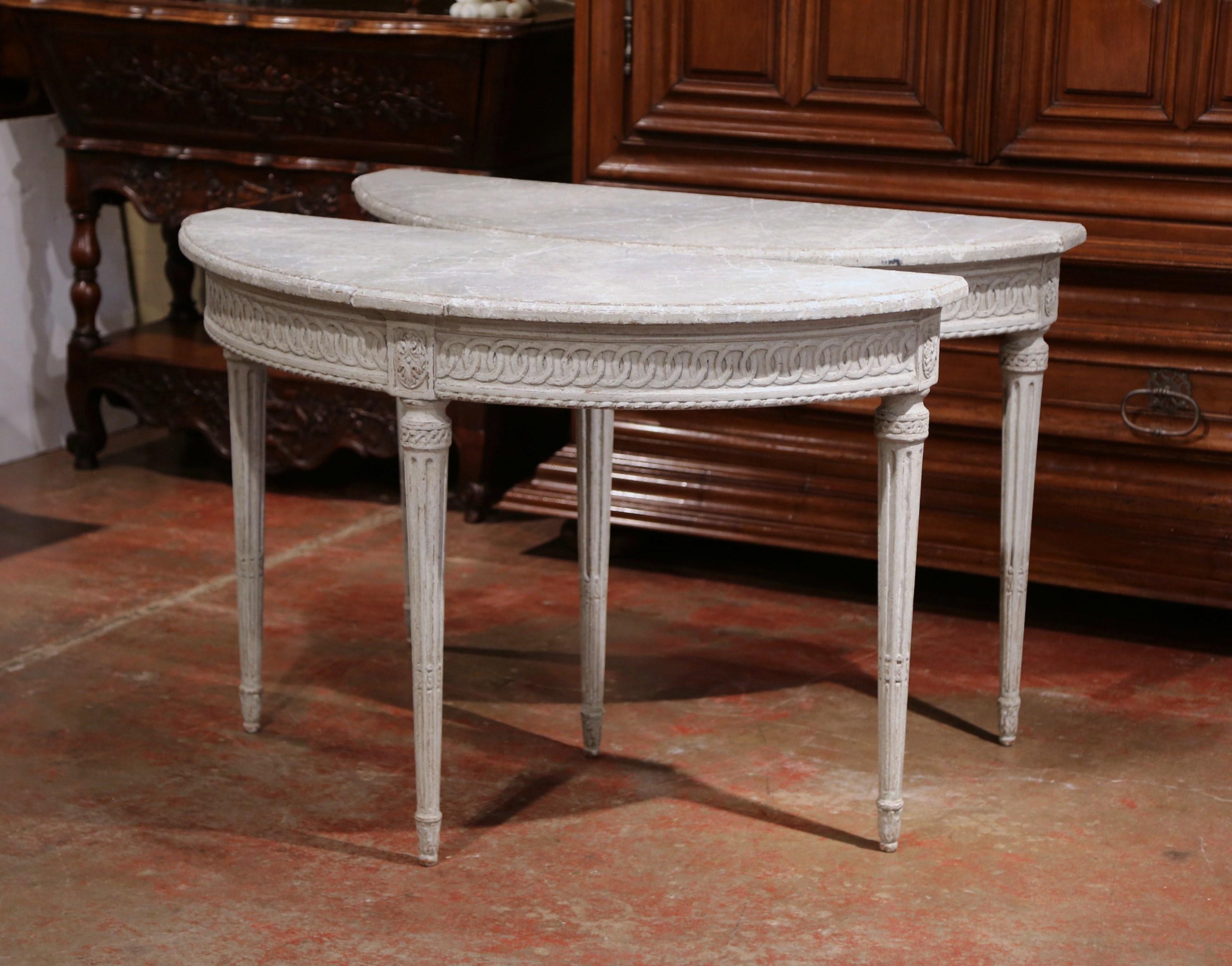 Decorate an entryway with this sophisticated pair of antique consoles. Crafted in northern France circa 1880 and shaped as half moon, each Louis XVI style table features three tapered and fluted legs, embellished with delicate carvings. The bombe
