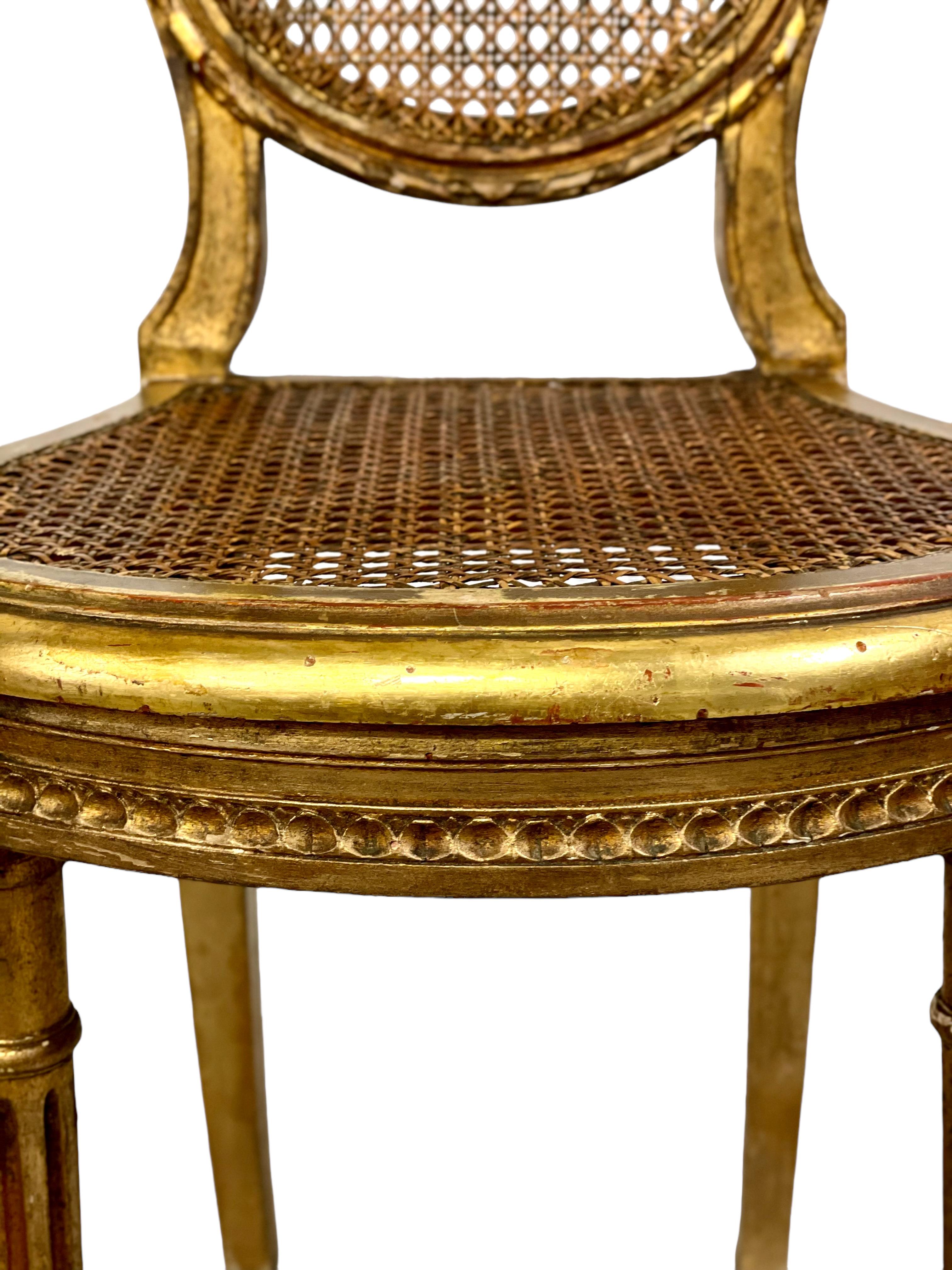 A matching pair of exquisitely gilded 19th century Louis XVI-style side chairs, with lightweight, caned oval backs and shaped and comfortable caned seats. The front legs are slender and carved, with fluted designs along their length and topped with