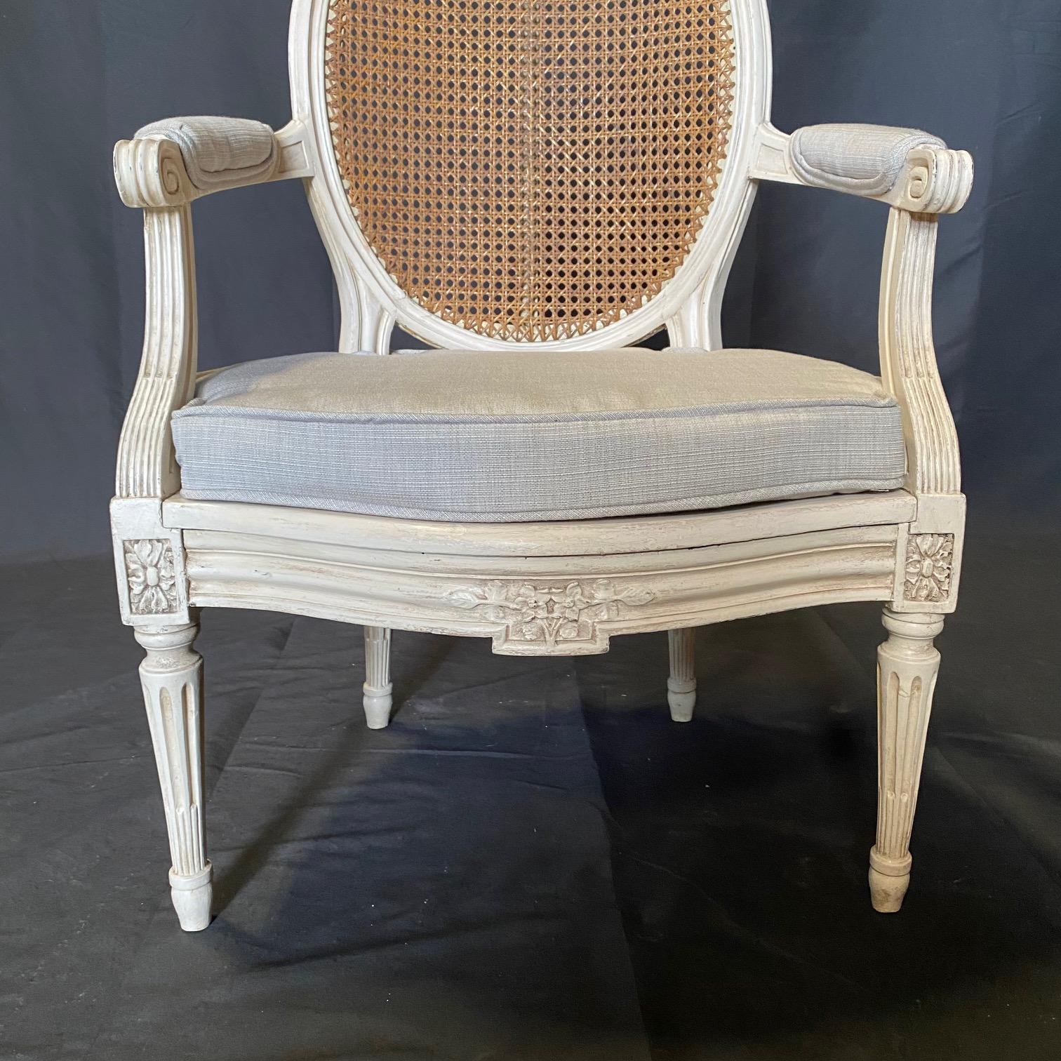 Très belle peinture ivoire sur cette paire de fauteuils ou chaises bergères avec un beau cannage en très bon état, et de nouveaux coussins d'assise et accoudoirs déhoussables. Jolie palette de couleurs neutres et la couleur vieillie de la peinture