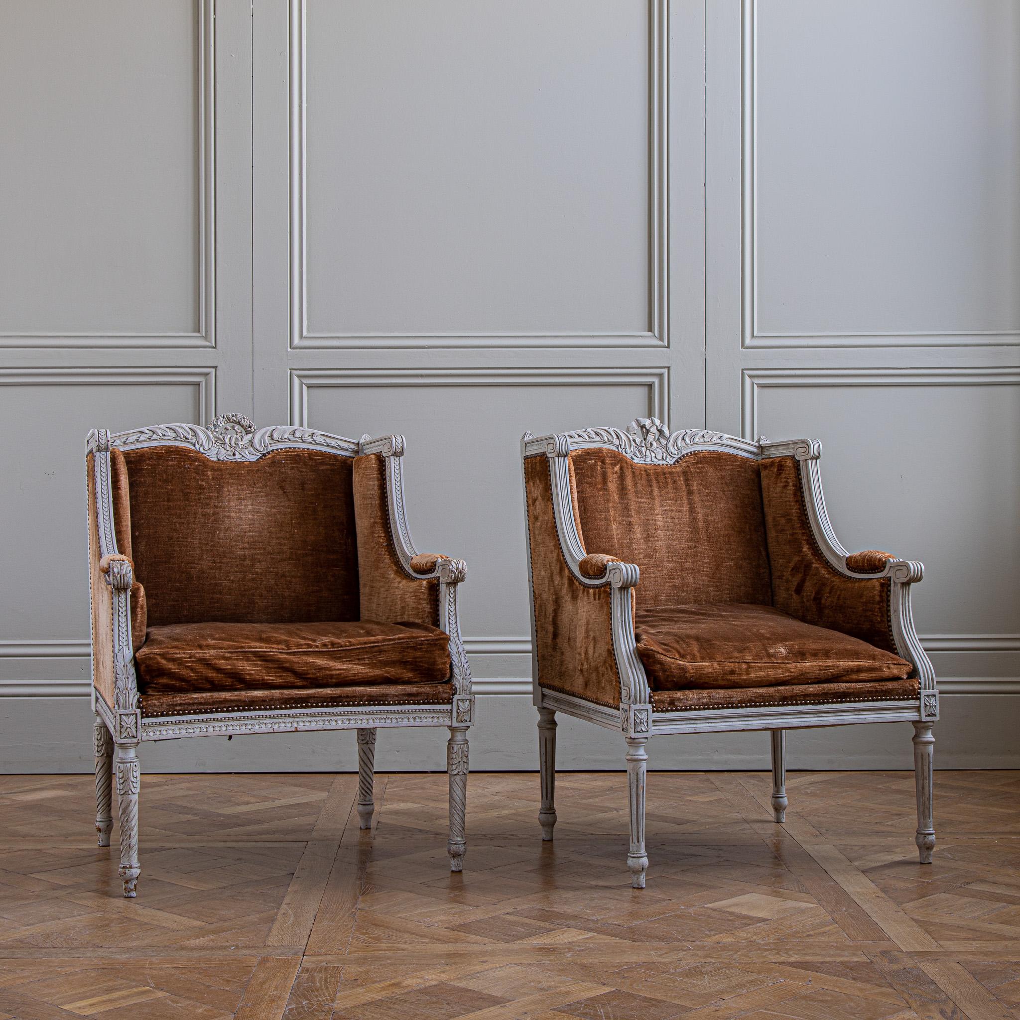 A pair of French Louis XVI style armchairs, 'bergères à oreilles', circa 1880. Created in France, during the 19th century. These chairs feature a wingback design with hand carved motifs of ribbons, flanked with petite flowers and foliage adorning