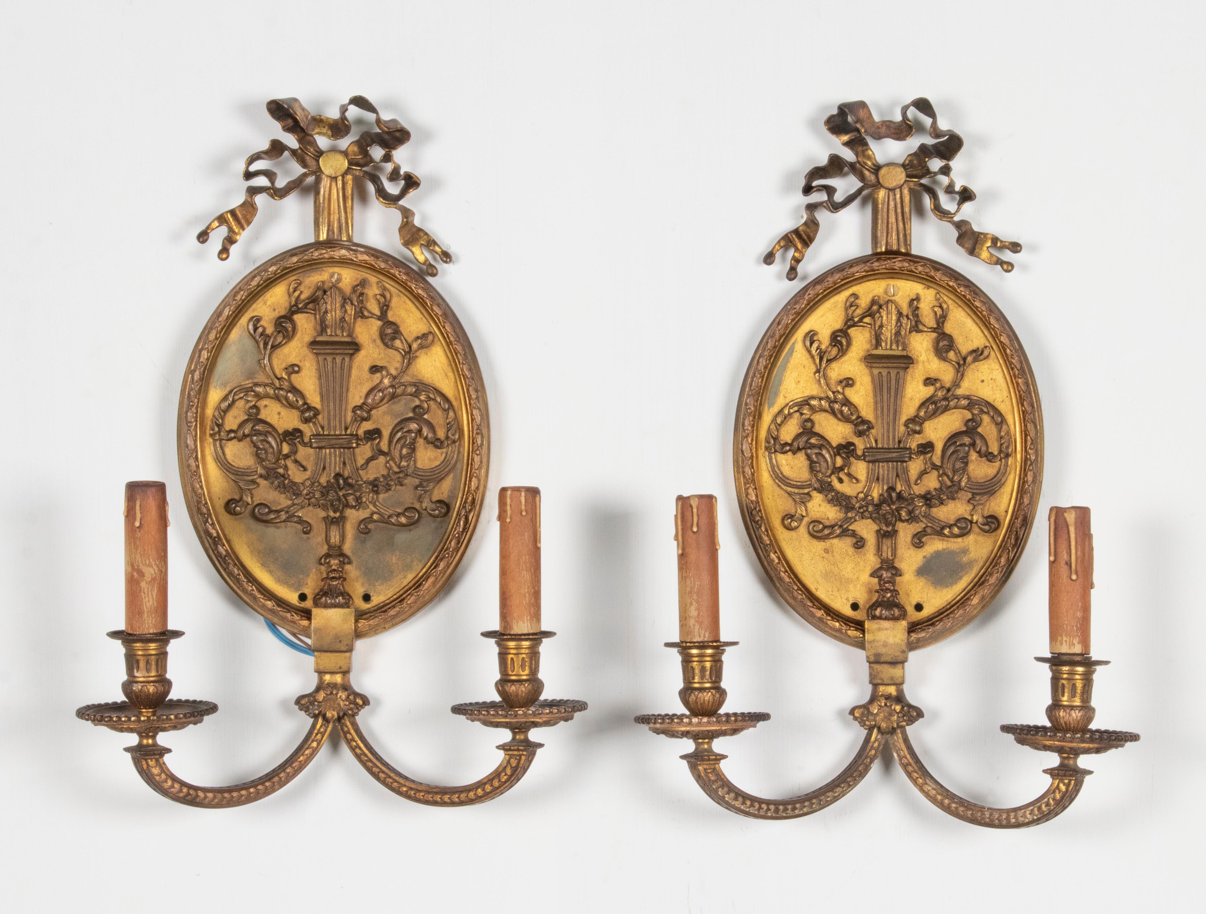 Beautiful antique wall sconces, made of bronze. Originally these were candlesticks and later they were made electric. The lamps have clear characteristics of the Louis XVI style, such as the large medallion shape and the bows at the top. The candles