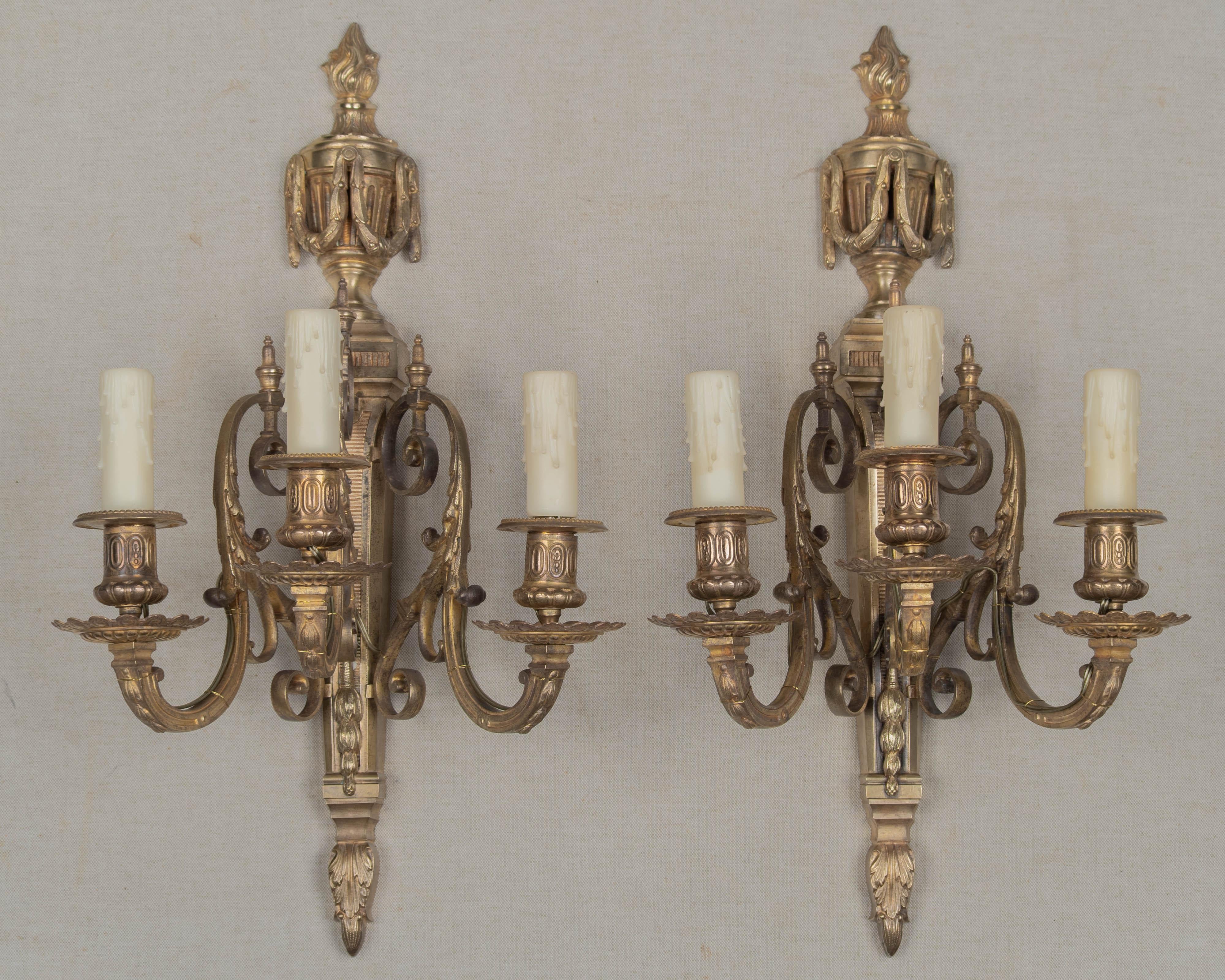 Paire d'appliques murales à trois lumières en bronze moulé de style Louis XVI du XIXe siècle. Lourdes appliques, joliment détaillées avec de grands bras à volutes avec des feuilles d'acanthe, une urne avec une flamme au sommet. Rééquipement avec de