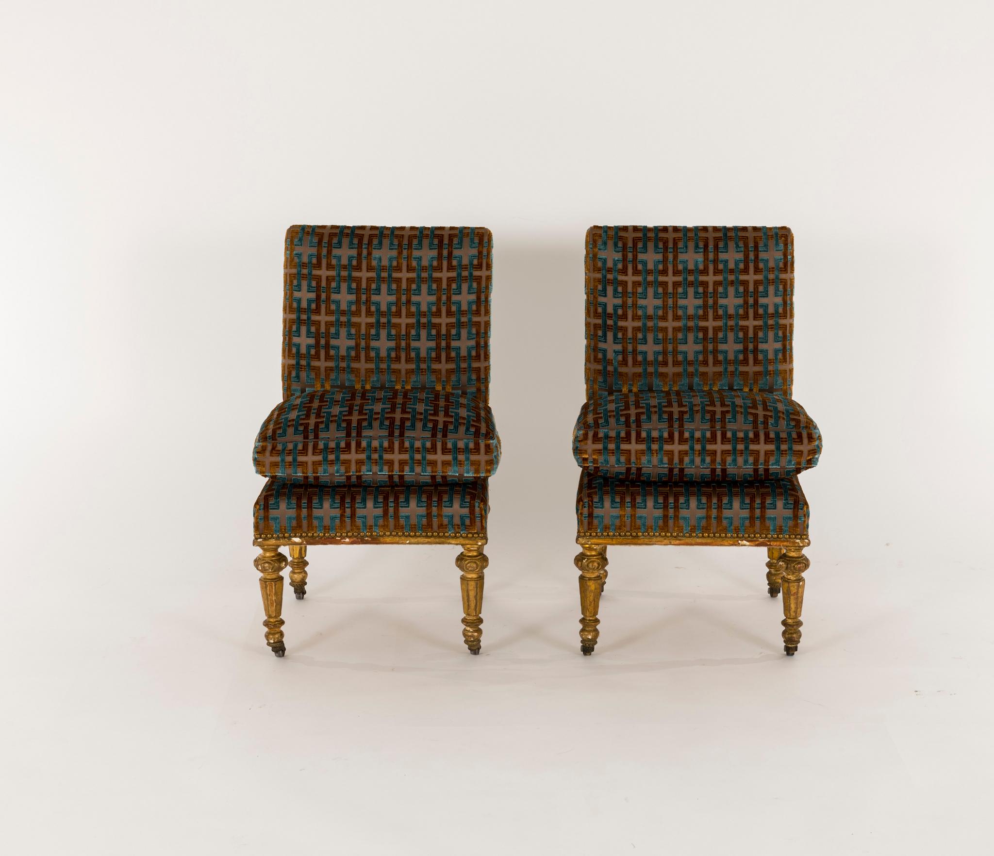 A striking Napoleon III giltwood chairs on casters, newly upholstered in a woven block chain velvet, chocolate leather trim, nailhead detail, and a lofty down seat cushion. Fabric is a cognac and Prussian blue velvet on a chocolate background.