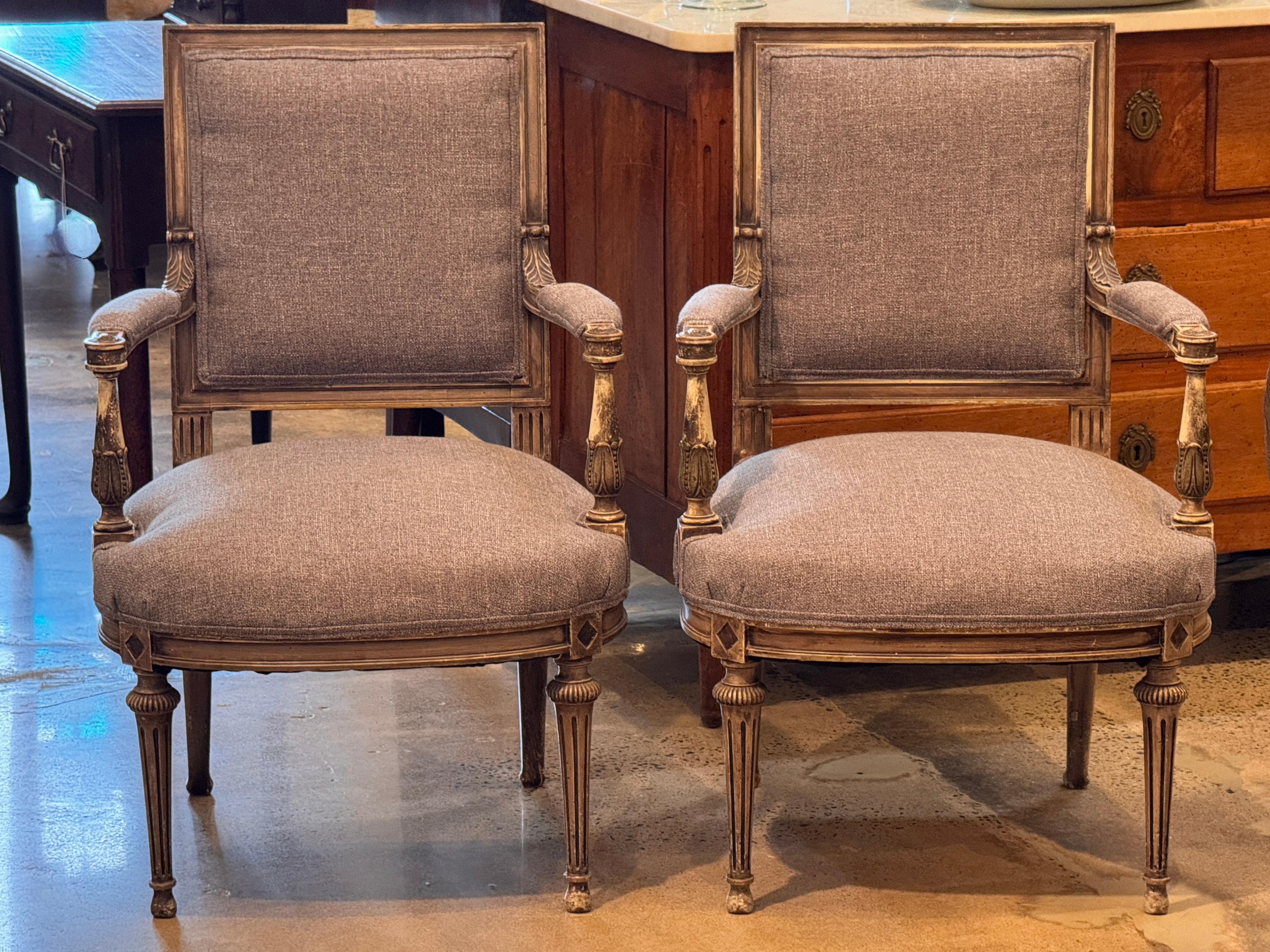 Ein Paar Sessel im Louis XVI-Stil, grau lackiert, mit geschnitzten, kannelierten Beinen und verschnörkelten Armen. Jeder Stuhl hat eine quadratische Rückenlehne und eine großzügige Sitzfläche, die mit einem strukturierten grauen Stoff gepolstert