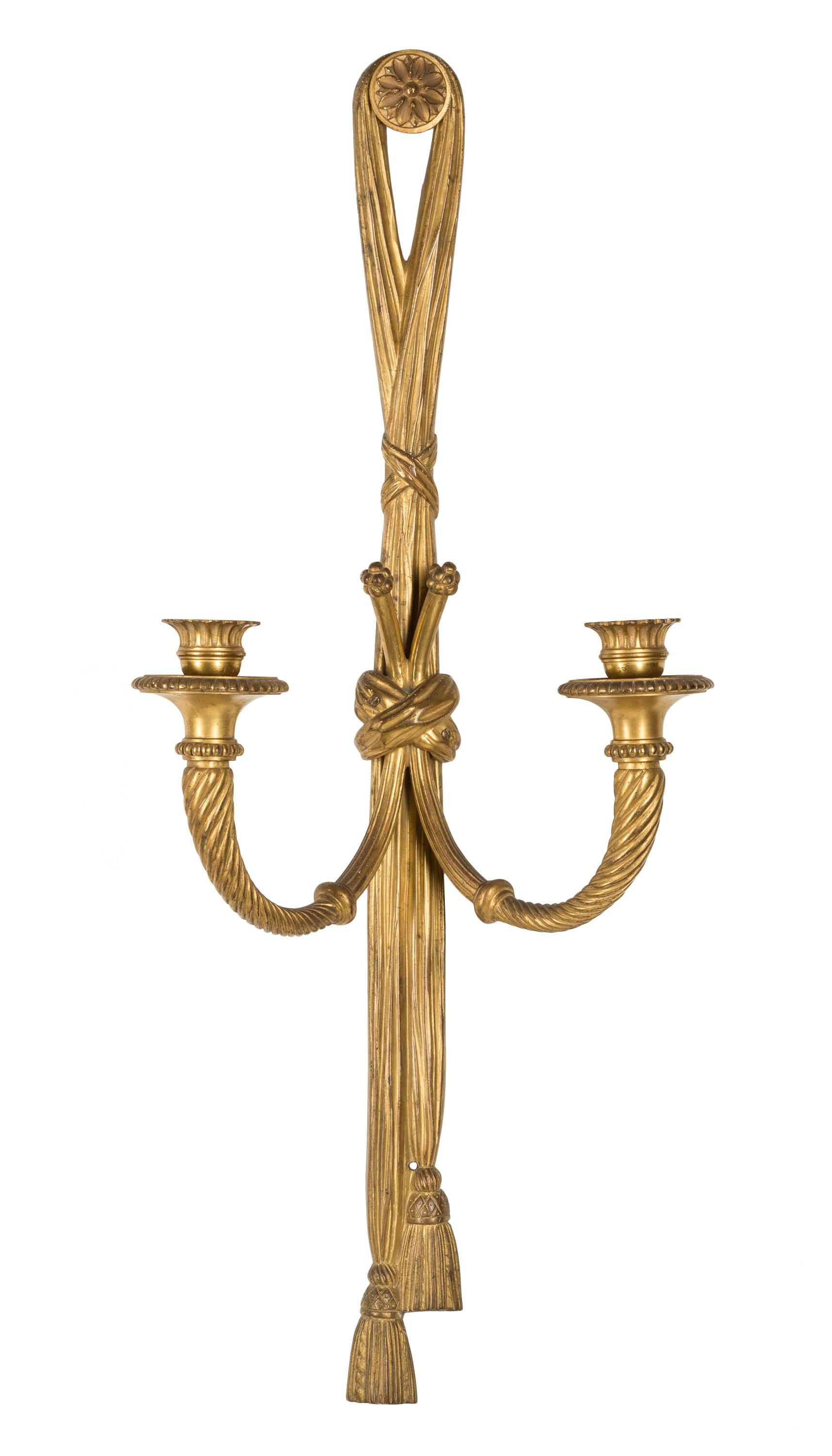 A matched pair of 19th century French gilt bronze wall sconces / appliqués in the form of knotted ribbons holding dual candle arms, ending in tassels, draped over buttons decorated with floral rosettes. These neoclassical elements, typical of the