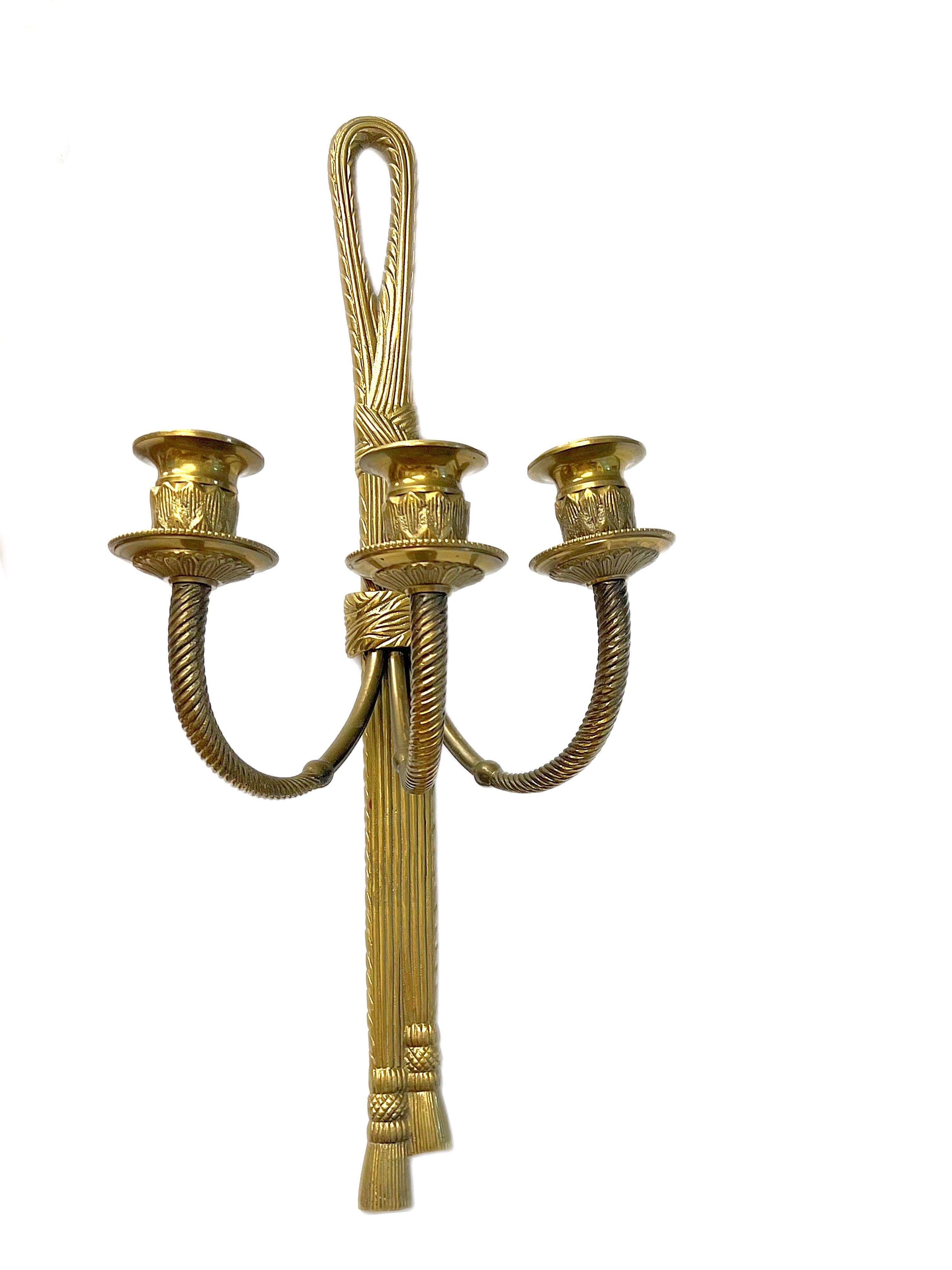 Asombroso par a juego de apliques de latón macizo con forma de cuerda y borlas y cintas anudadas que sostienen dos brazos de vela. Estos asombrosos conjuntos se fabricaron en el siglo XIX en Francia.  Ambas piezas notables terminan en borlas,
