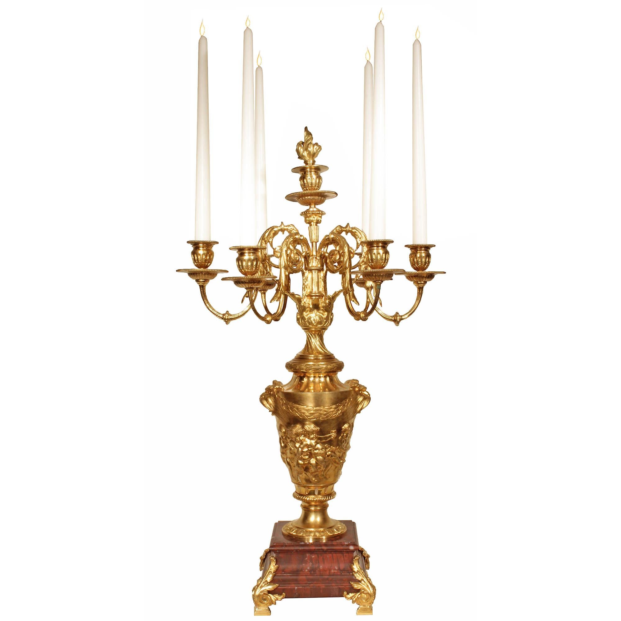 An exquisite pair of 19th century Louis XVI style ormolu and marble candelabras. Each candelabra is raised on a square Rouge Griotte marble base on ormolu feet with acanthus leaf ormolu mounts. Above, each superbly chased ormolu urn portrays a