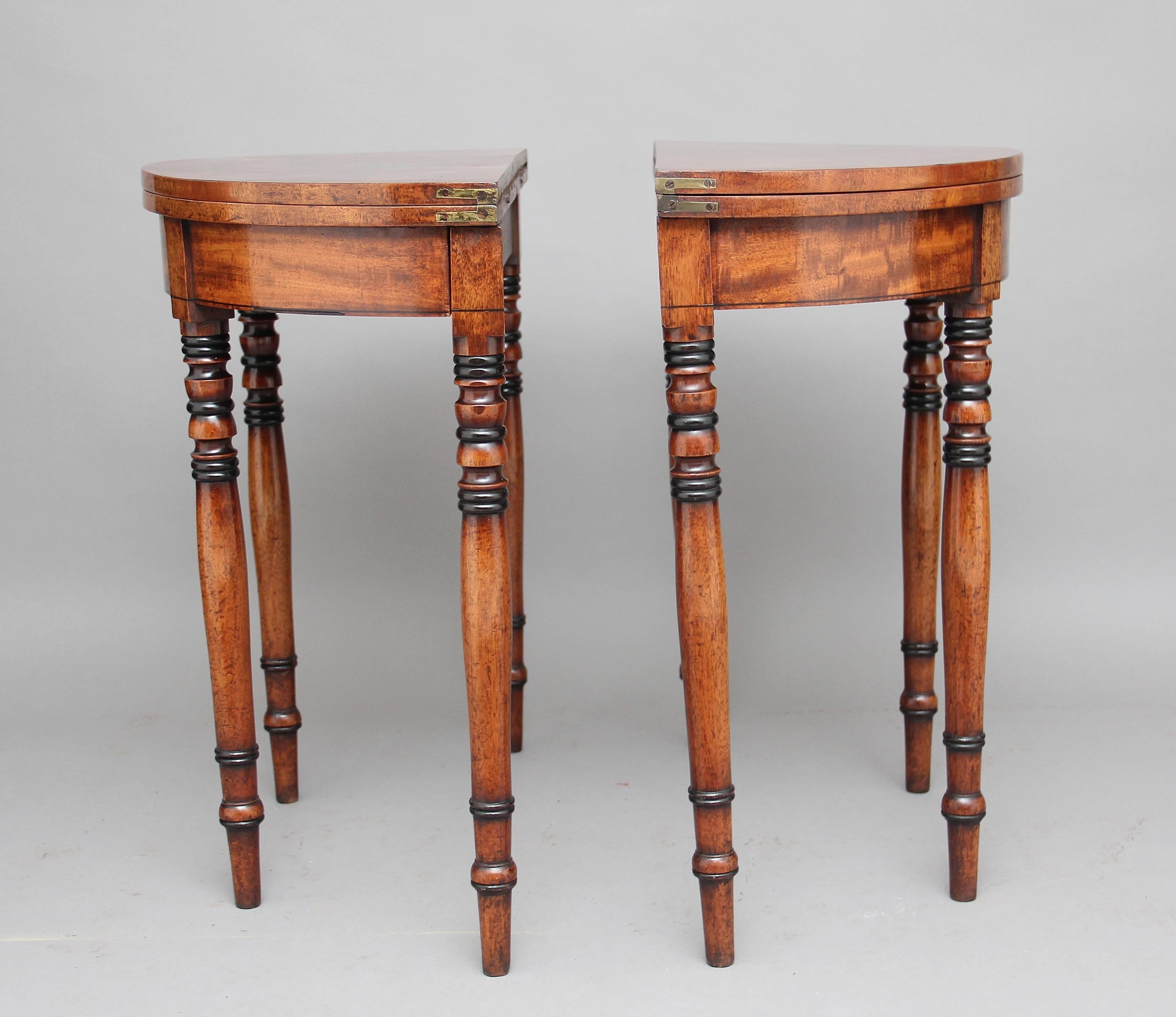 A pair of 19th century mahogany demilune card tables, the semi circular tops opening to reveal a green baize playing surface, with a frieze below supported on nicely turned legs which are partly ebonised, circa 1840.
 