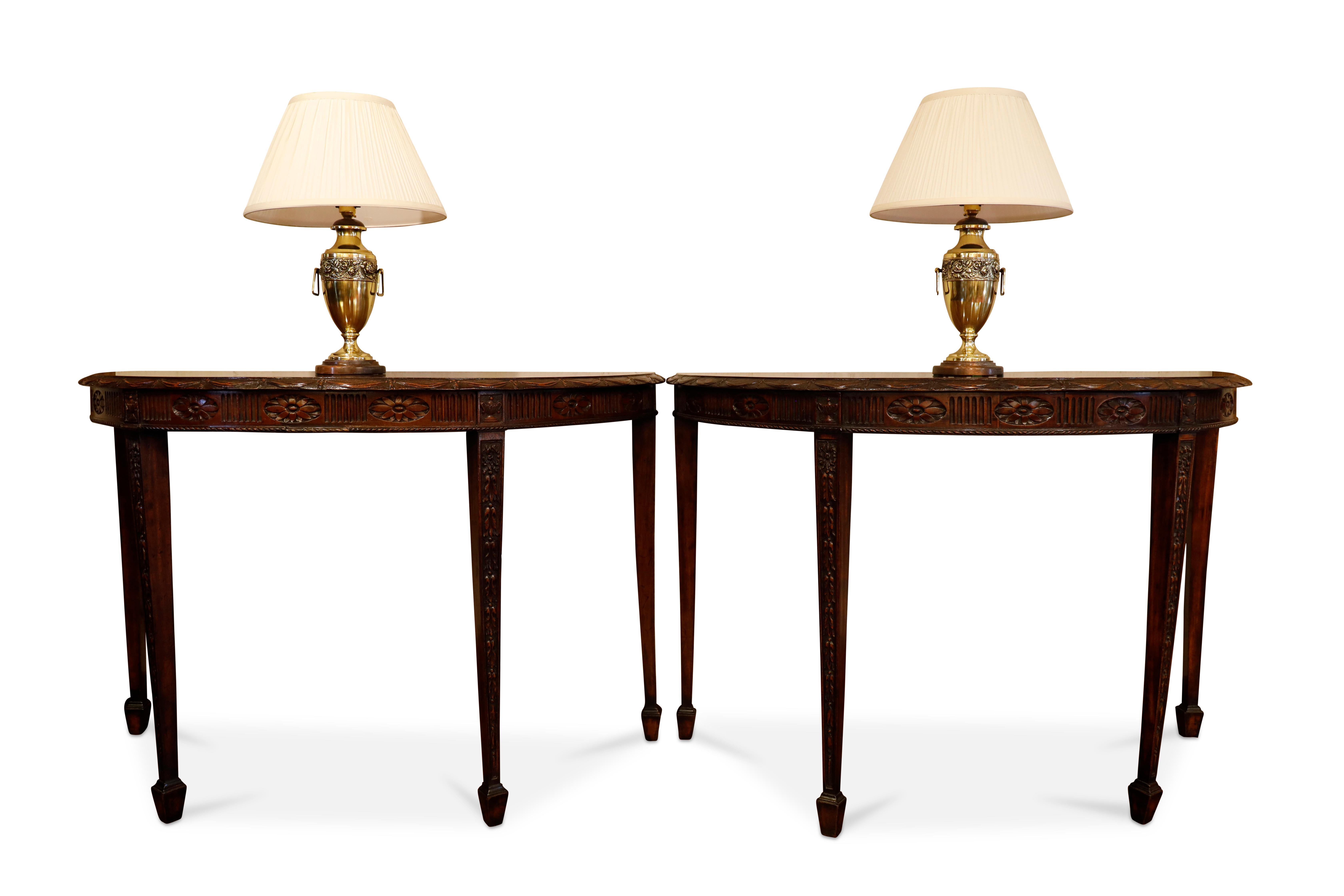 Paire de tables démilunies en acajou anglais avec des sculptures complexes.  Le bord est orné d'une guirlande et le freize présente un motif floral avec des urnes encadrées au-dessus de chaque pied.  La table repose sur des pieds fuselés avec des