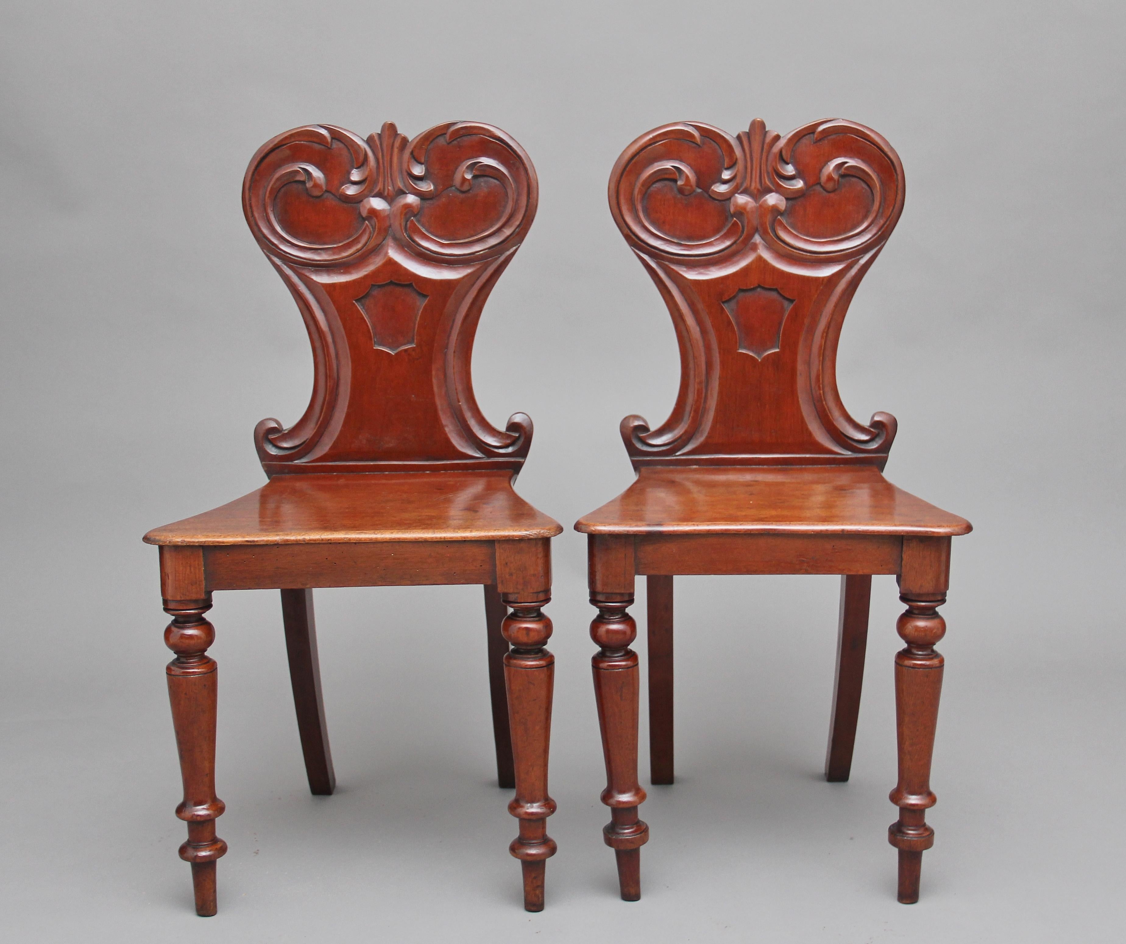 A pair of mid-19th century mahogany hall chairs, having shaped backs carved with scrolling acanthus and centred by shield reserves, supported on out swept rear legs and turned front legs, circa 1840.