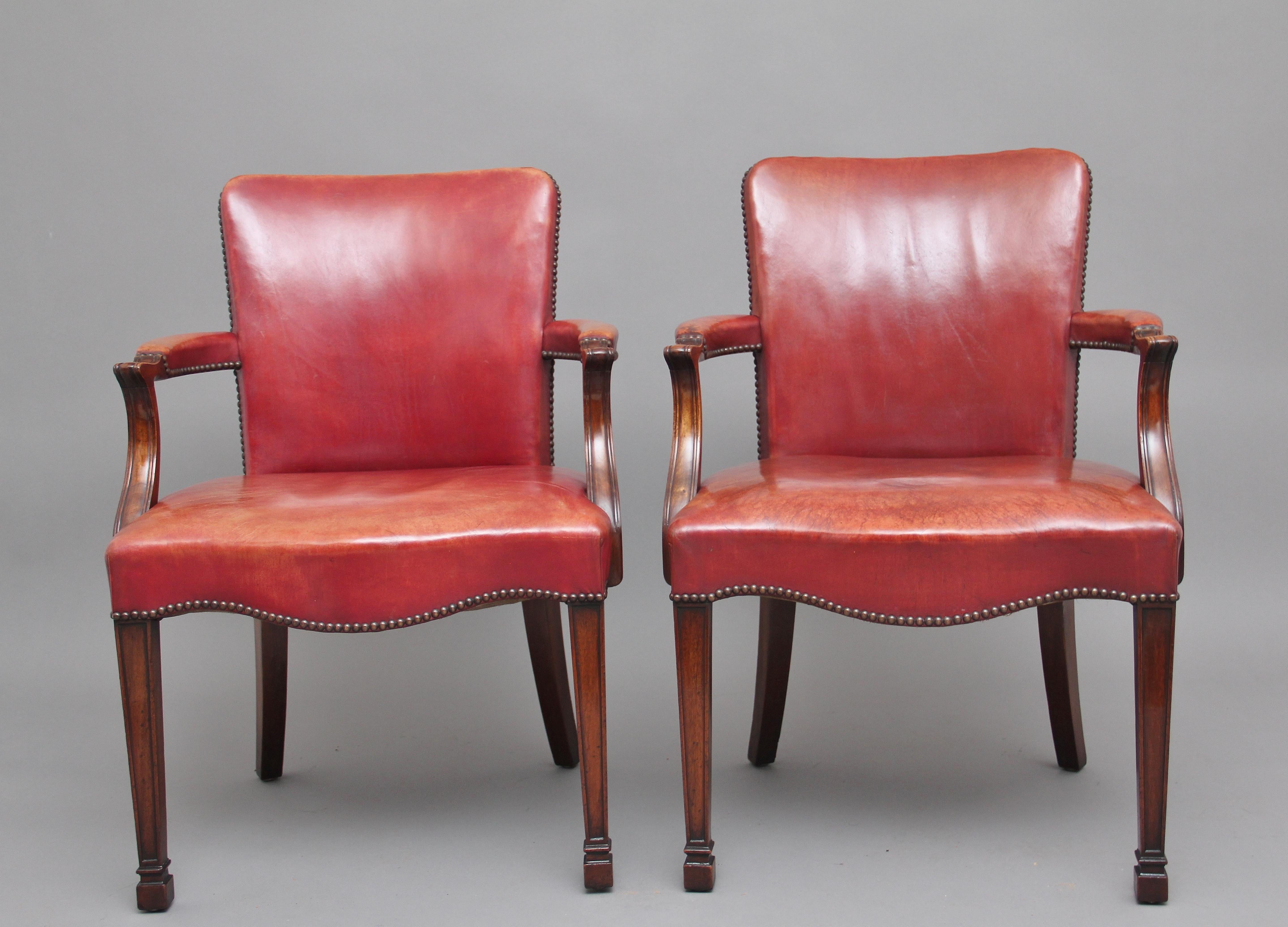 A pair of 19th century mahogany library armchairs upholstered in faded red leather with brass stud decoration, with shaped backs and scrolling arms over serpentine seats, supported on panelled square tapering legs ending in spade feet, circa 1890.