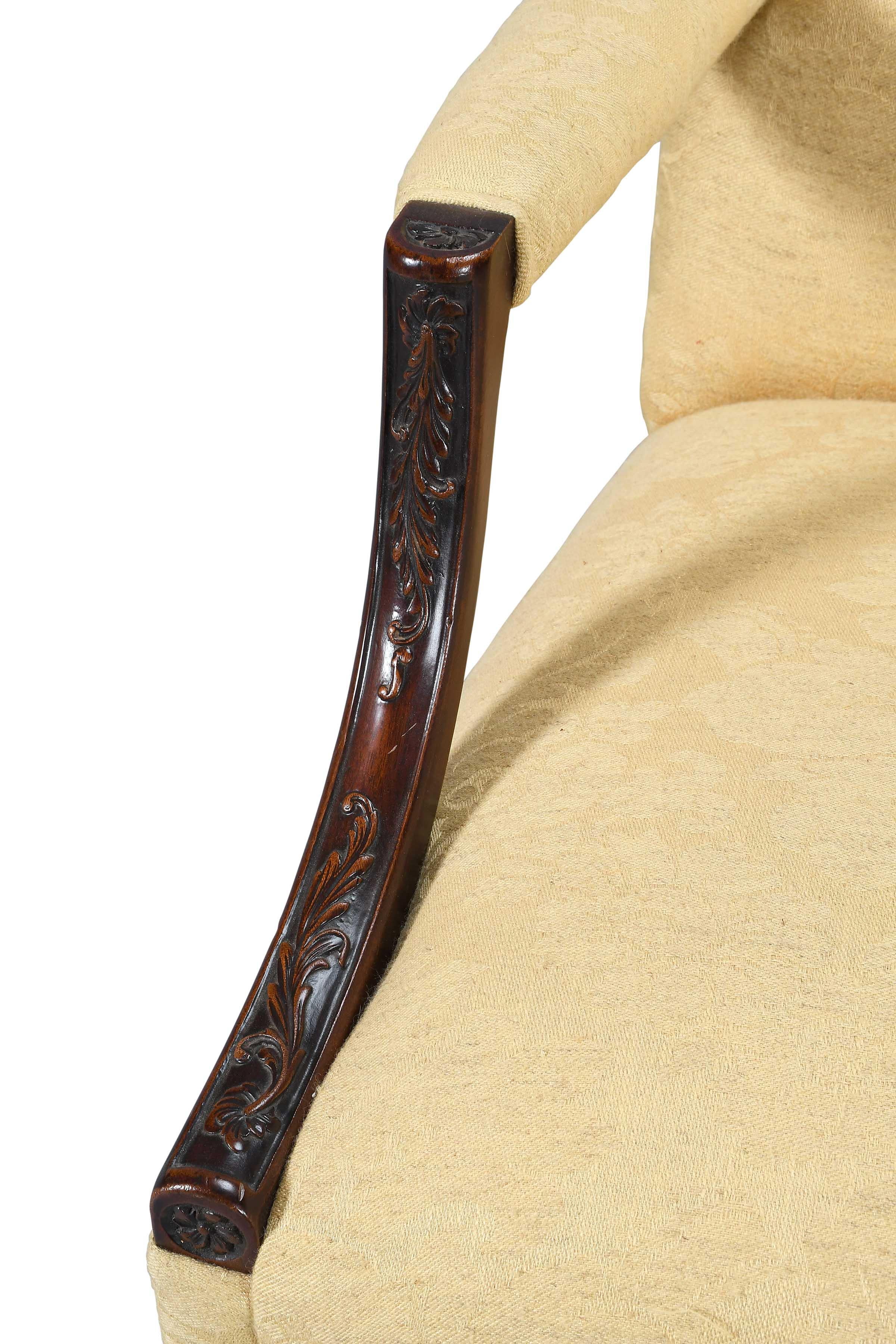 A pair of mahogany 'Gainsborough' chairs with foliate carved arm supports and front legs adorned with blind fretwork. Well upholstered with arched, padded backs. The legs connected by stretchers and raised on later brass casters. Comfortable and