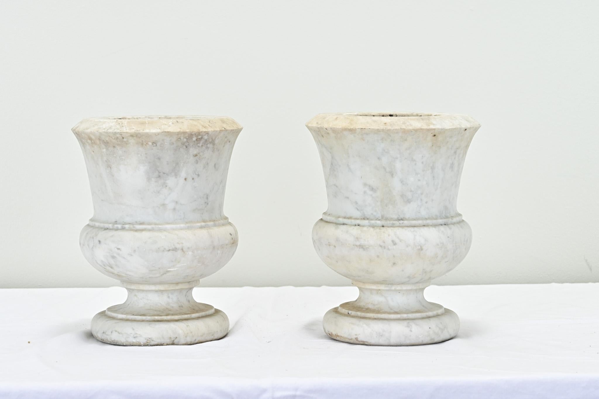 A French pair of heavy urns hand chiseled from one piece of marble. The smooth and worn marble is full of patina. Perfect for styling your mantle or other table top needing a pair. The interior is carved out measuring 5 ¾” H x 4” Diameter. Be sure