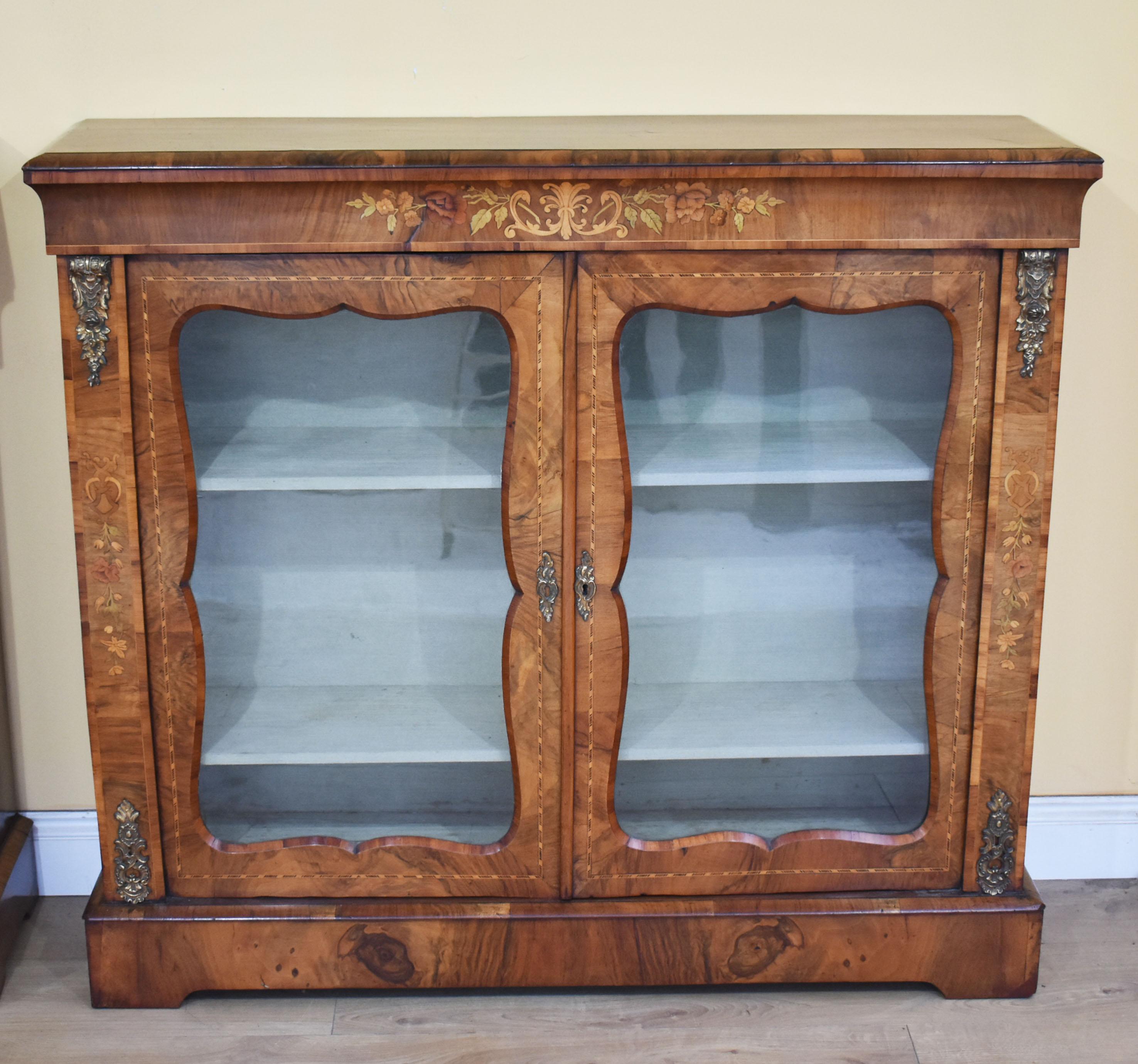For sale is a good quality pair of Victorian walnut pier cabinets. Each cabinet having floral marquetry inlay above the glazed doors, opening to reveal a fabric lined interior with two shelves. Each door is flanked by ormolu mounts at the top and