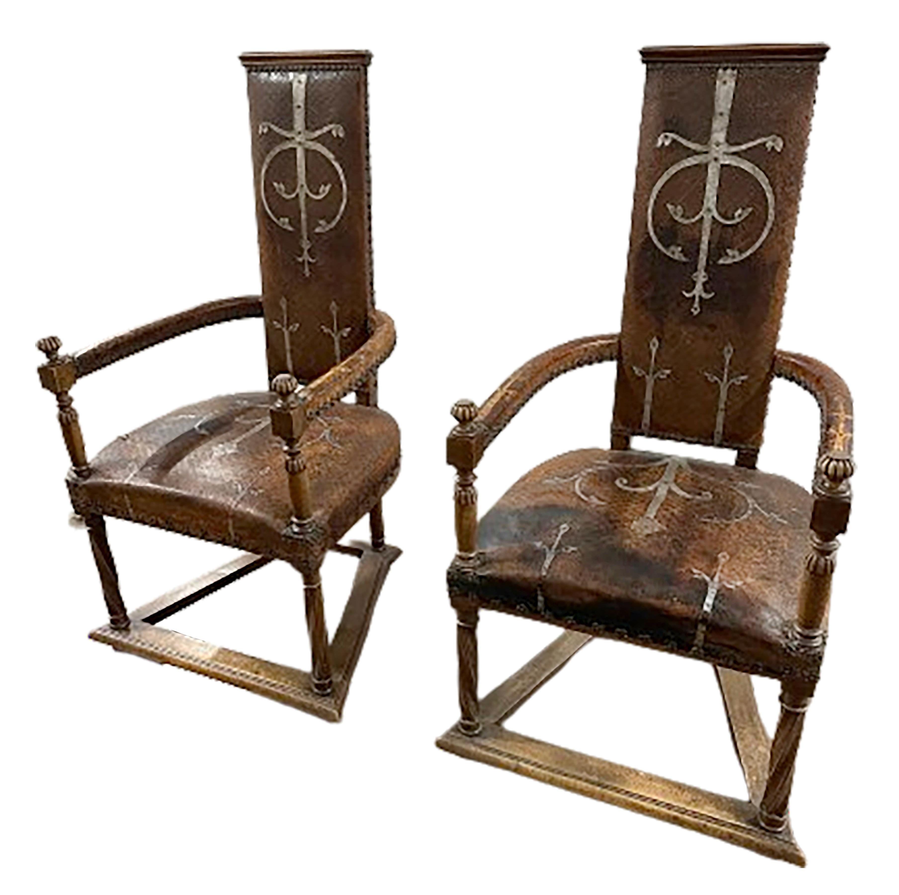 An exquisite pair of Mid-19th Century studded leather Spanish armchairs. Featuring tall, slender backrests crowned with subtle arches and grand out-swinging arms, each chair is adorned with chocolate-colored leather upholstery embossed and silver