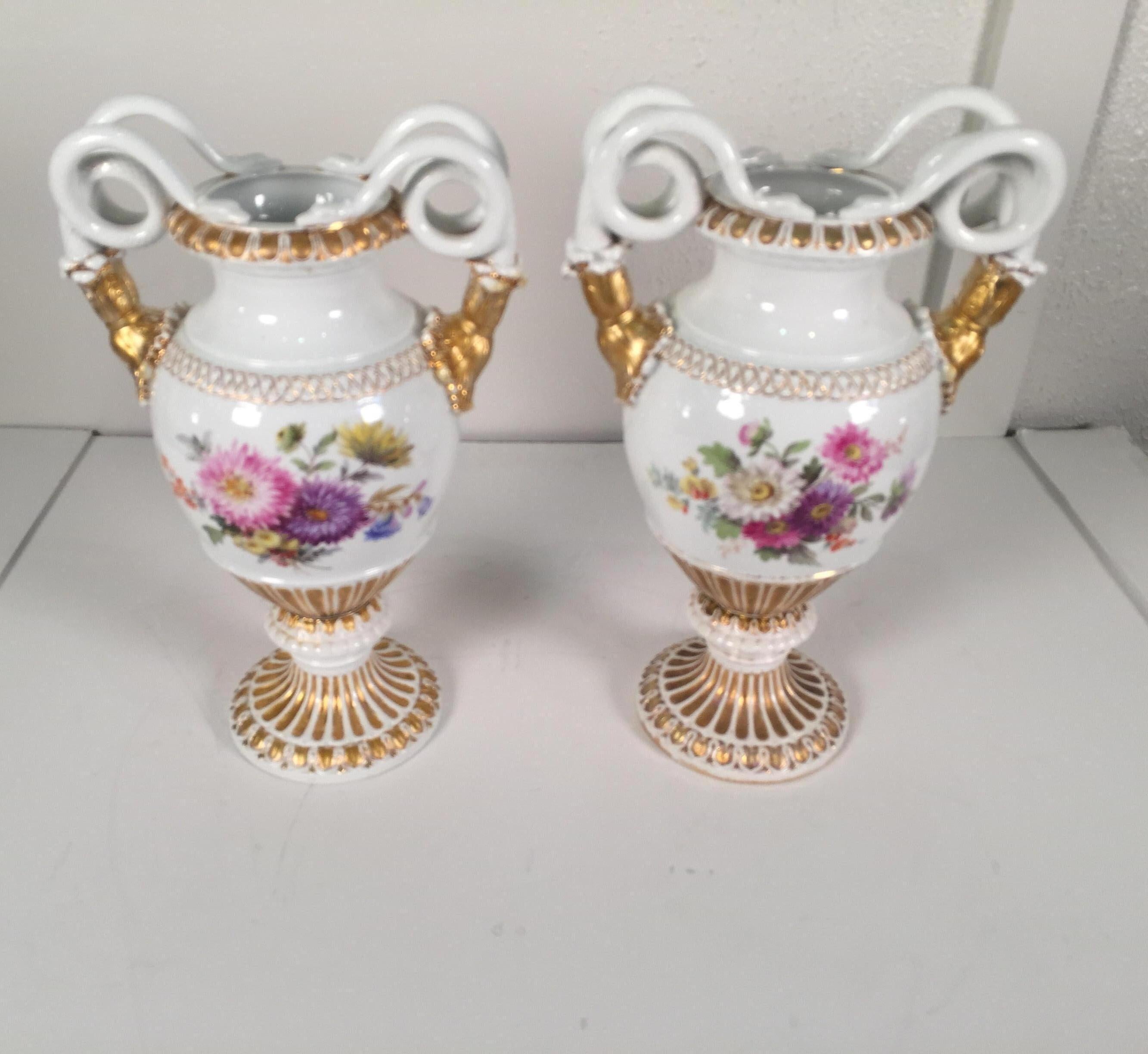Classic pair of German porcelain hand painted and gilt Meissen snake handled urns. The hand painted floral back and front with different floral bouquet cartouches with gilt handles and pedestal bases. Each one with the Meissen cross swards mark in