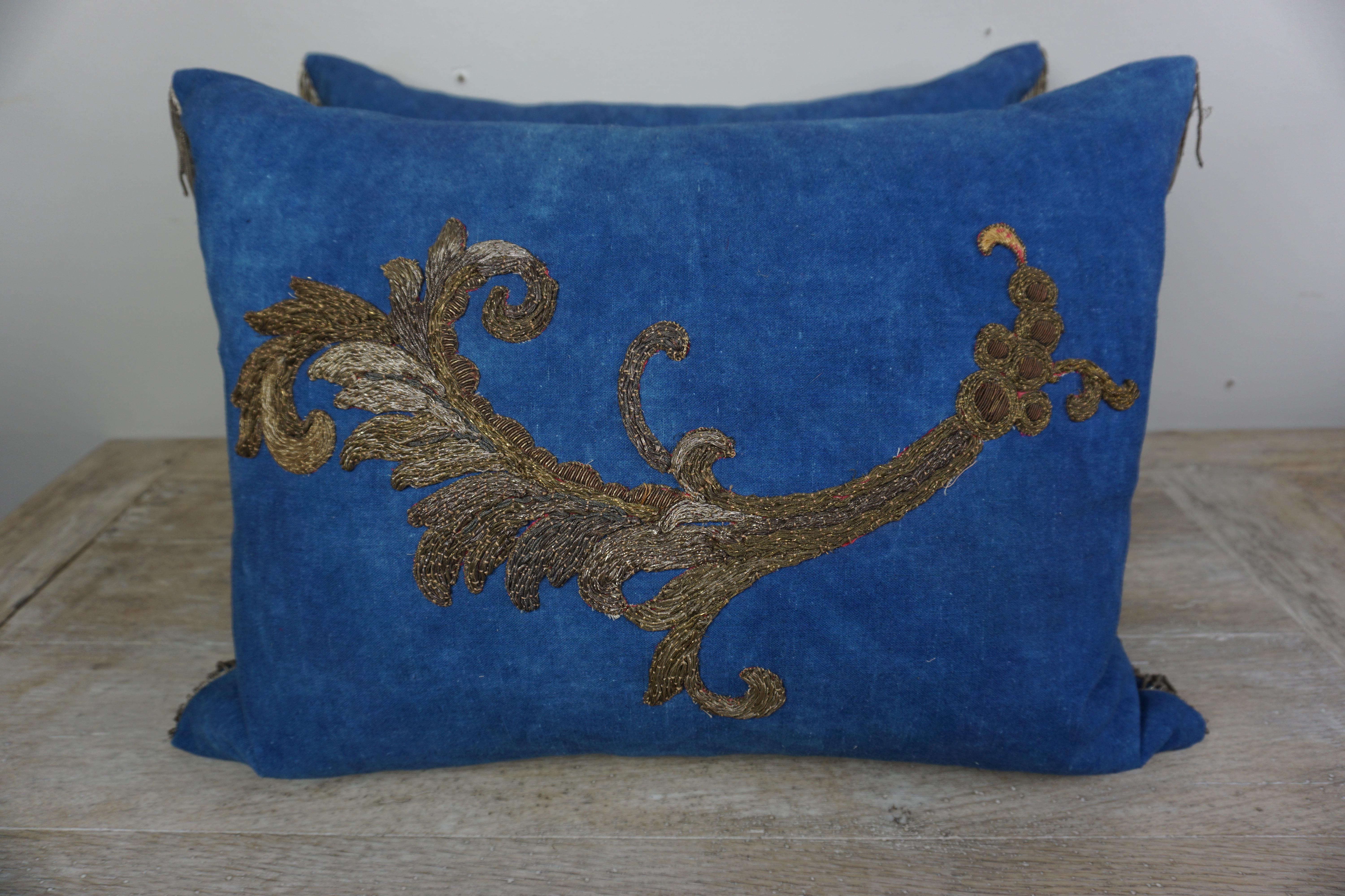 Pair of custom pillows by Melissa Levinson. 19th century gold and silver metallic appliques on blue linen fronts with blue linen backs. 19th century metallic trim at sides of pillows. Down inserts, sewn closed.