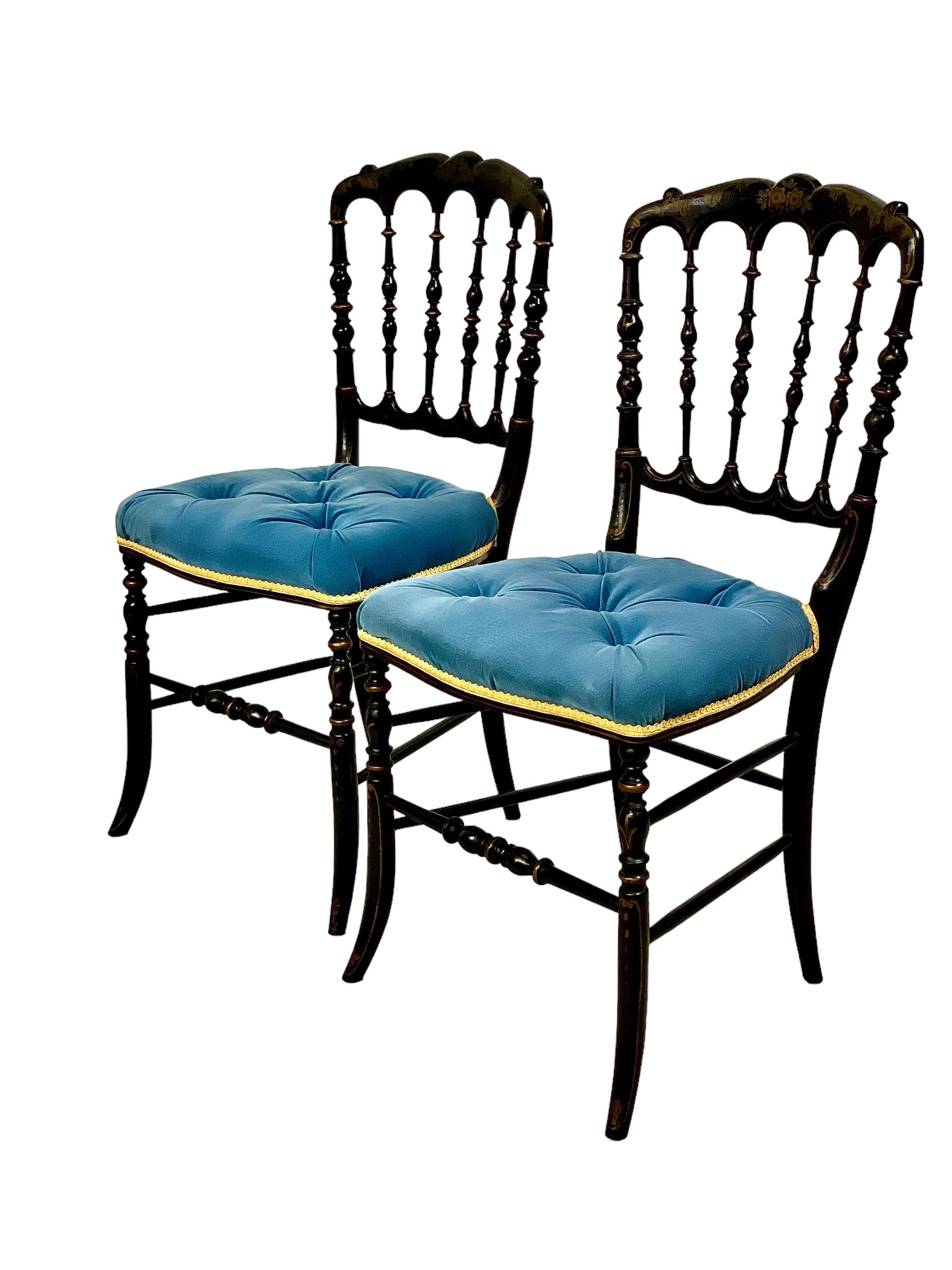 A gorgeous pair of 19th century Napoleon III opera chairs in ebonised wood, each with a wonderfully ornate spindle back and a gilded decoration of flowers and foliage on the top rail. A comfortable tufted seat in blue velvet is bound all round with