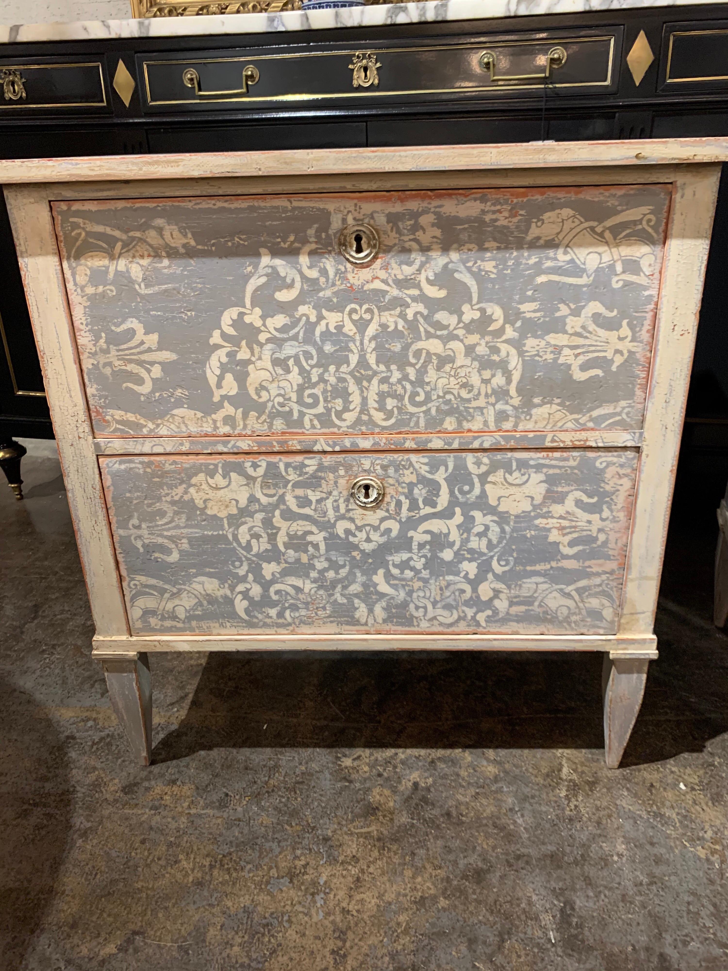 Beautiful pair of painted 2-drawer bedside tables. This set has a lovely decorative neoclassical design painted in grey on the drawers. Very unique! Note: There is a chest of drawers with pattern as well if you want to complete the set.