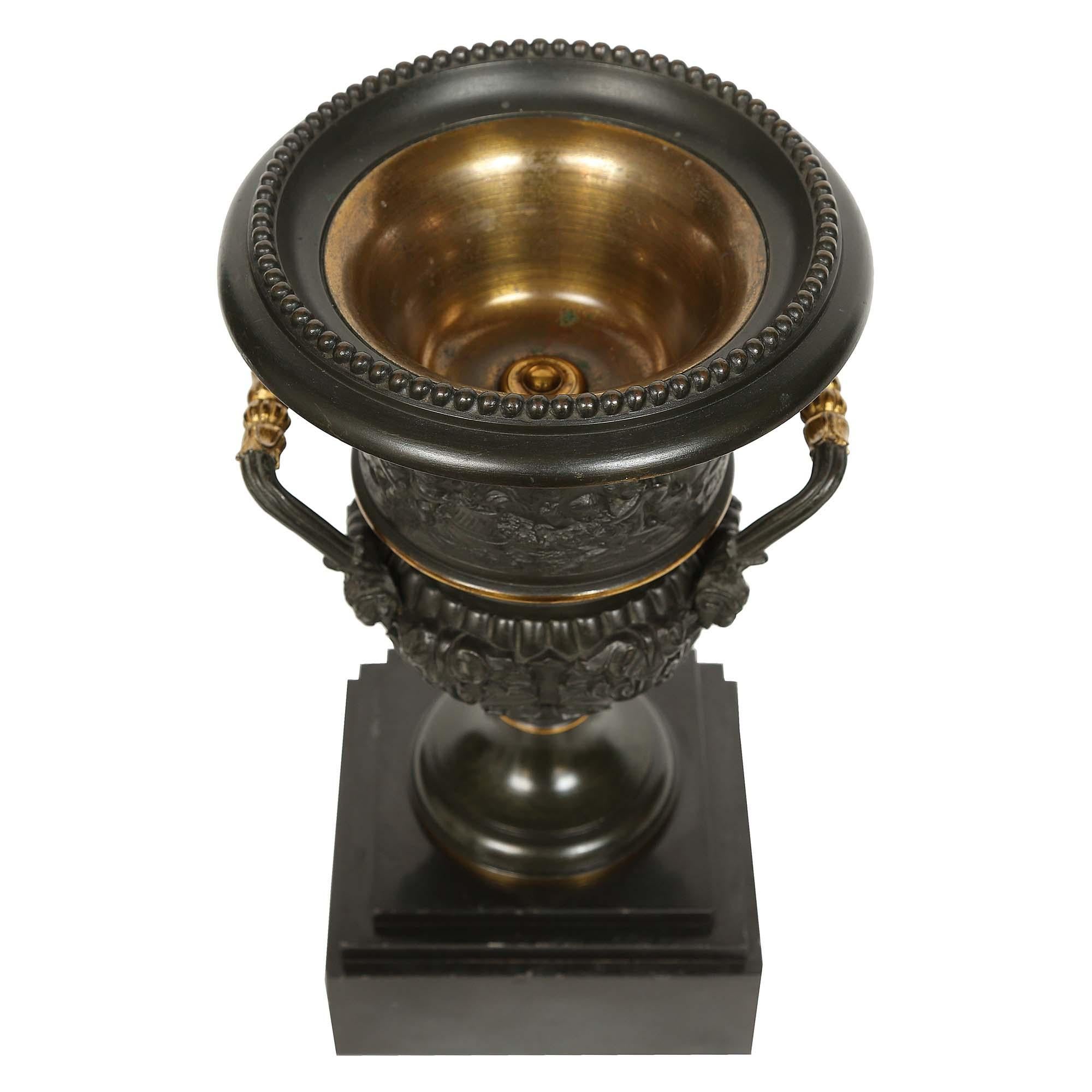 Una coppia molto attraente di urne in bronzo neoclassiche del XIX secolo. Ogni urna poggia su una base quadrata in marmo nero belga dai bordi screziati. Sopra c'è l'urna in bronzo patinato con bordi e rifiniture in bronzo dorato e disegni fogliacei
