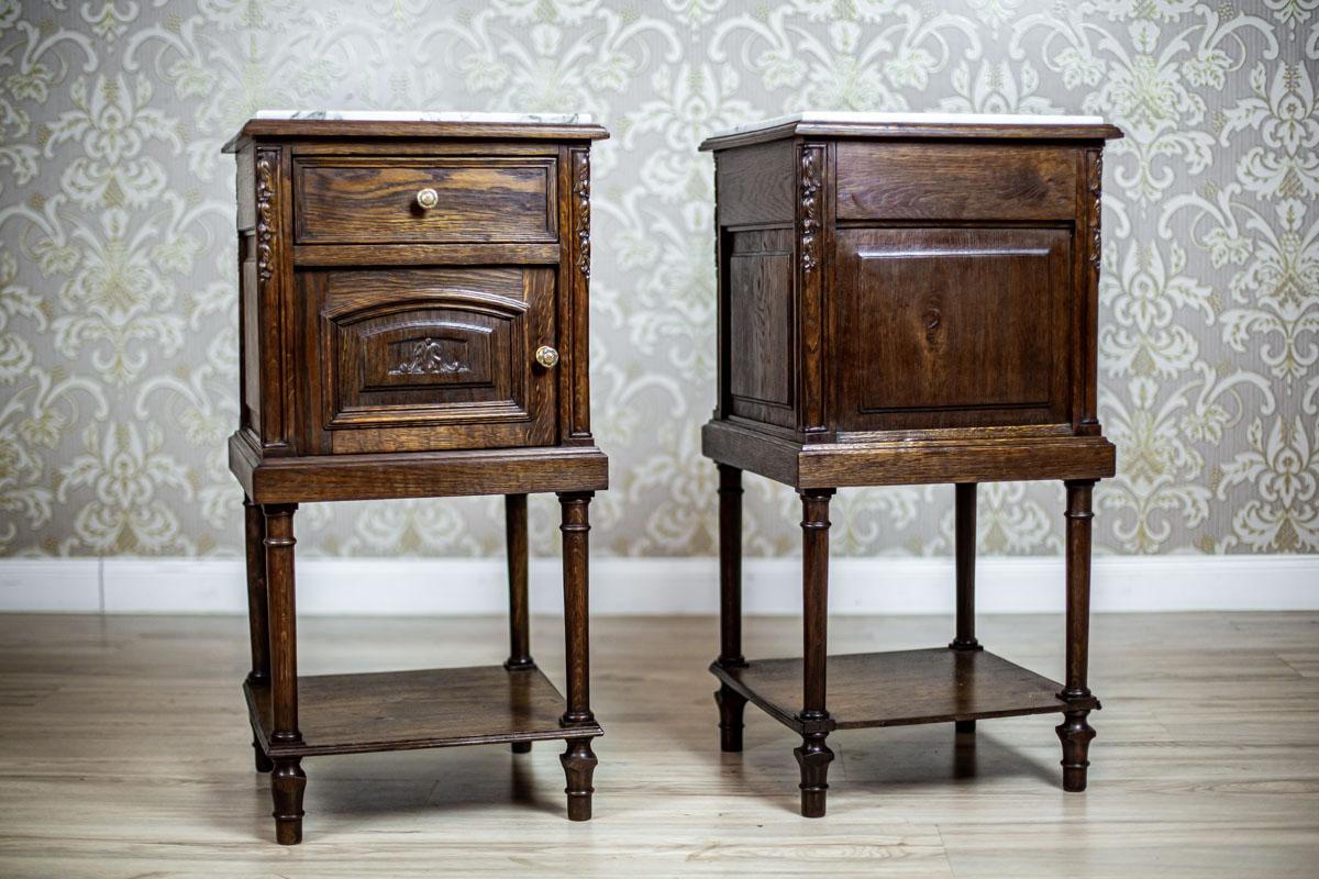 We present you two oak nightstands with a white marble top.
The furniture is from the late 19th century.
Each piece has a drawer under the top and a single-leaf cabinet.
Furthermore, the nightstands are supported on high, thin legs, which are