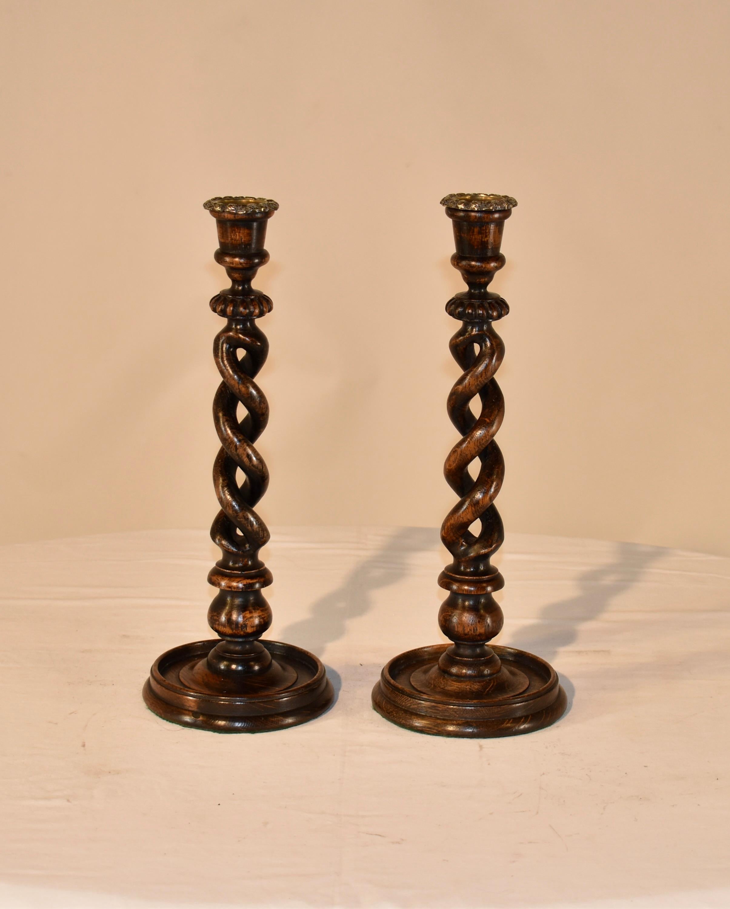 Pair of 19th century oak candlesticks from England with open barley twist stems. This pair of candlesticks has hand cast brass bobeches over hand turned candle cups, supported on wonderfully hand turned open barley twist stems with hand carvings at