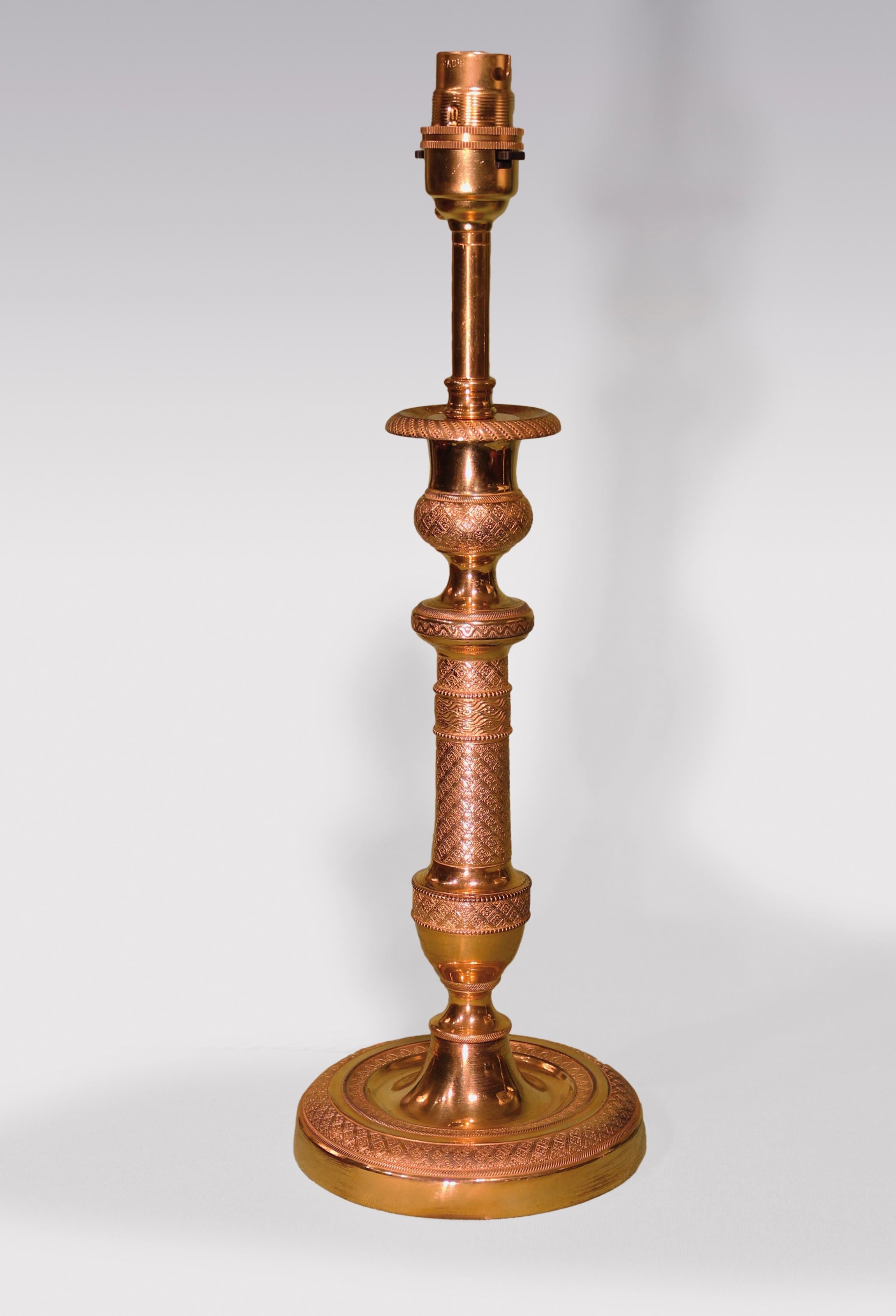 A pair of early 19th century ormolu candlesticks intricately engine turned throughout, having vase-shaped nozzles above tapering stems with urns below supported on circular bases. (Now converted to lamps.)