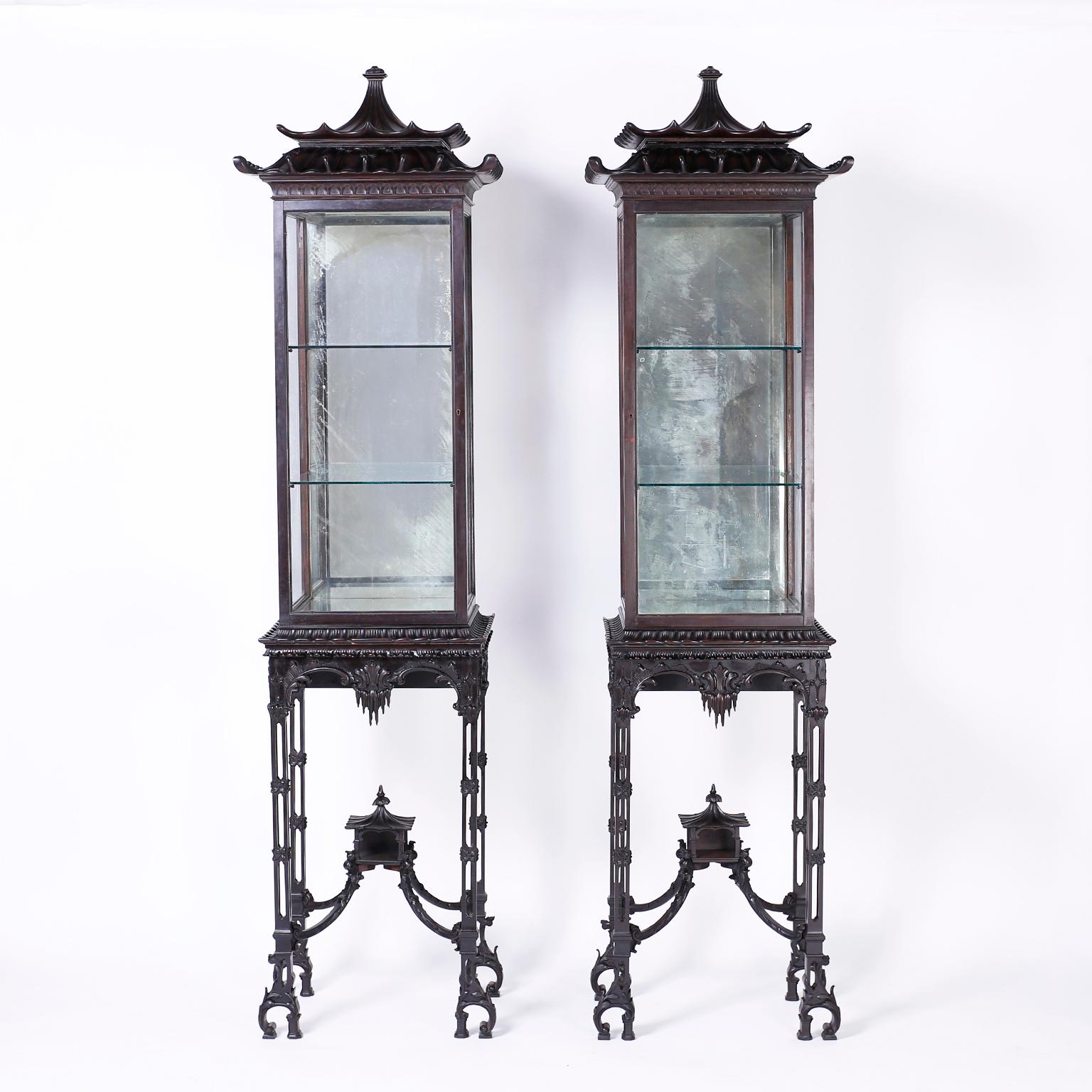 Pair of antique mahogany display cases that are a stunning example of the Chinese Chippendale style. Having pagoda tops over a glass case with glass shelves and a mirrored background. The elaborate carved bases have classic oriental legs supported