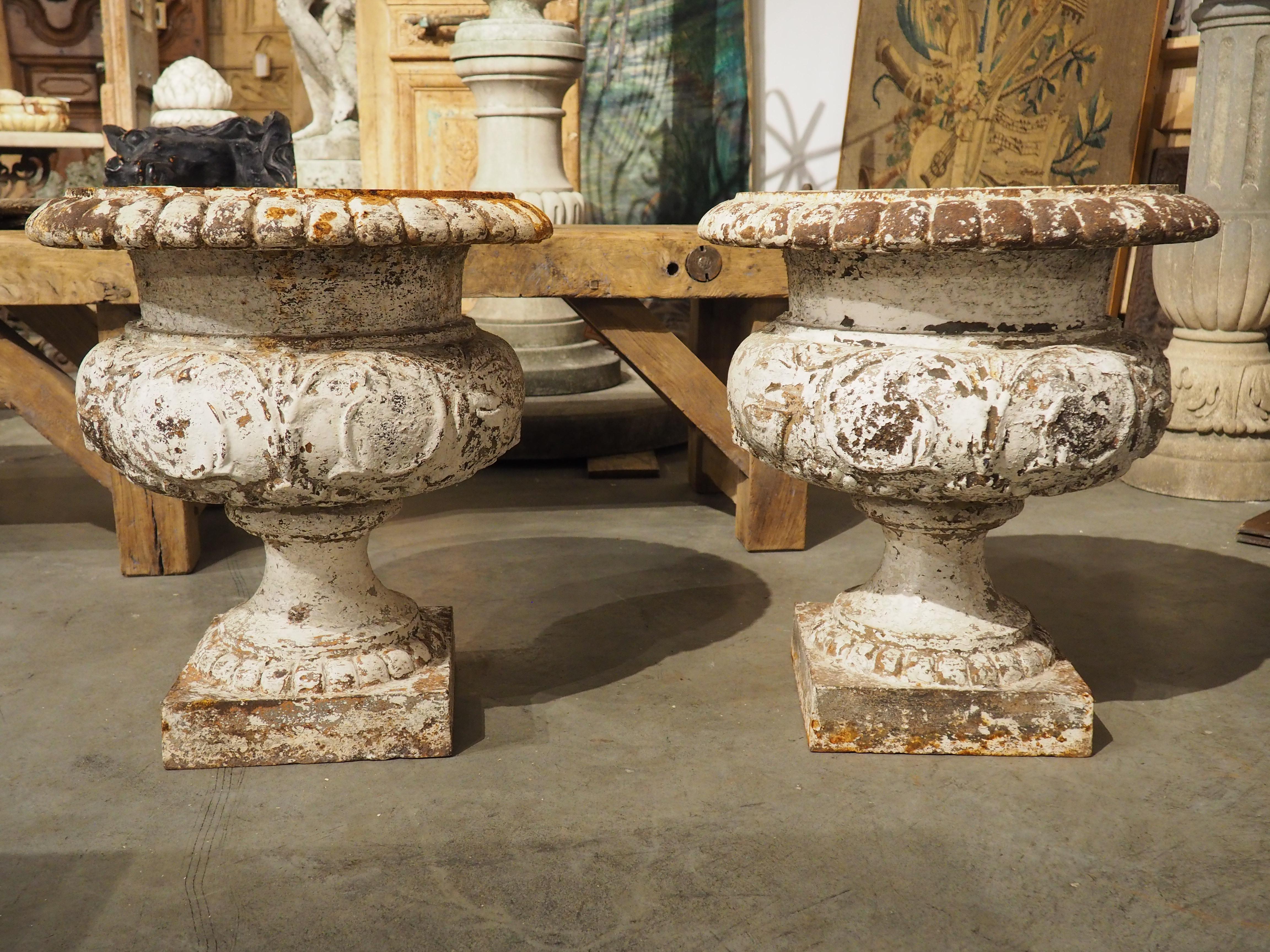 Originaria della Francia, questa coppia di vasi in ghisa è perfetta come fioriera per interni o esterni. I vasi, che risalgono al 1800, sono stati dipinti di bianco; tuttavia, le perdite di colore che caratterizzano la vernice hanno portato a zone