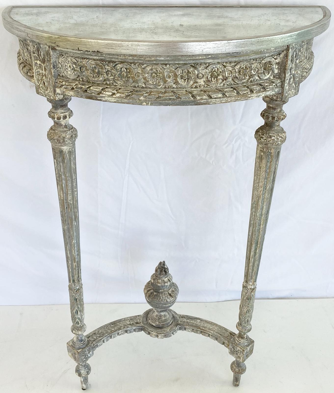 Pair of Louis XVI style, painted and parcel silvergilt demilune wall-mounting consoles, each top of mirrorplate on antique table base with fielded apron, out-carved with evolute scroll and gadrooing, raised on two round, fluted, tapering legs,