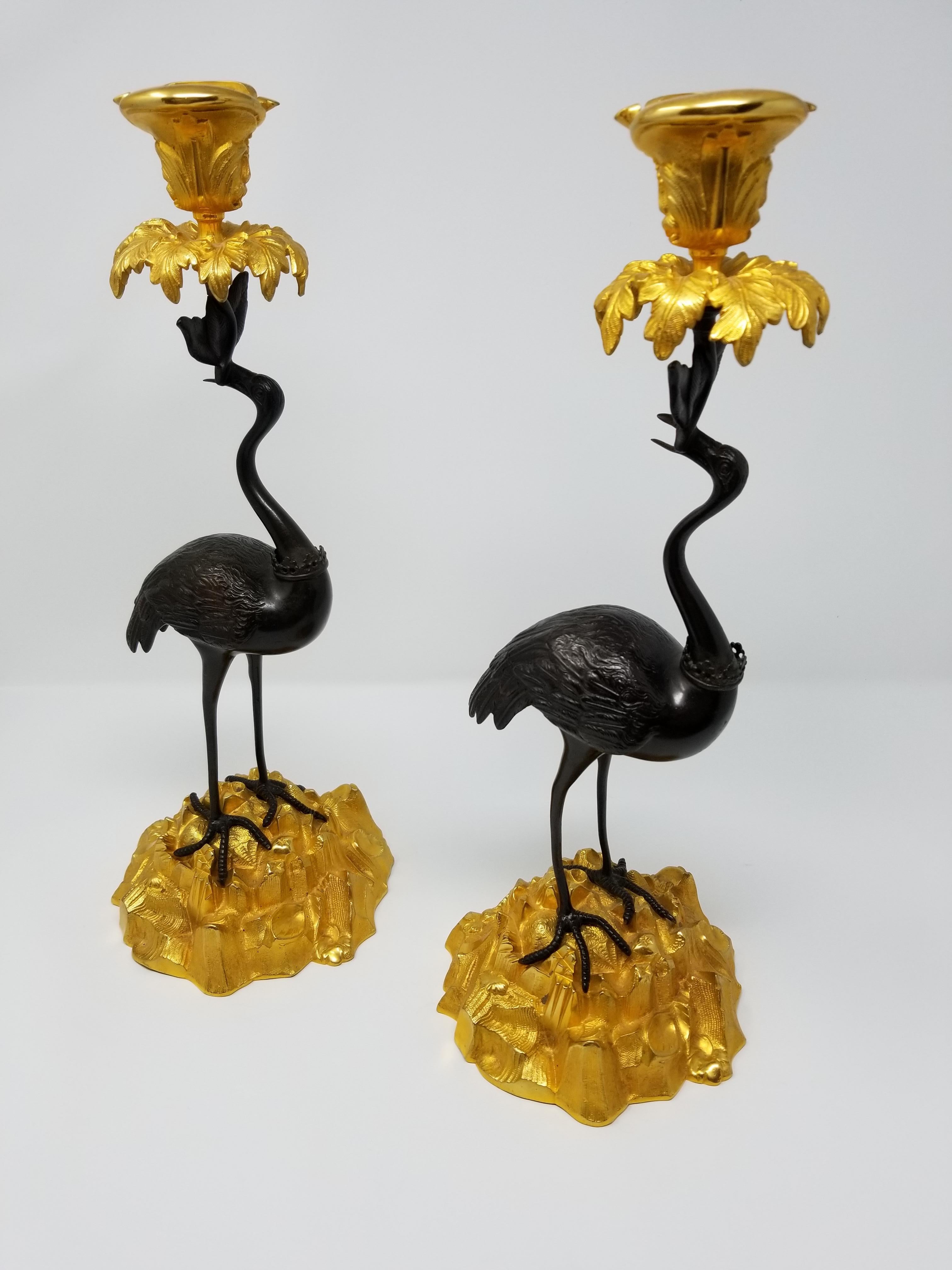 A beautiful pair of French chinoiserie patinated and gilt bronze standing crane-form candlesticks. Each crane is beautifully hand-chiseled with exceptional detail from the feet to the feathers and head. The cranes are seen standing on a beautifully