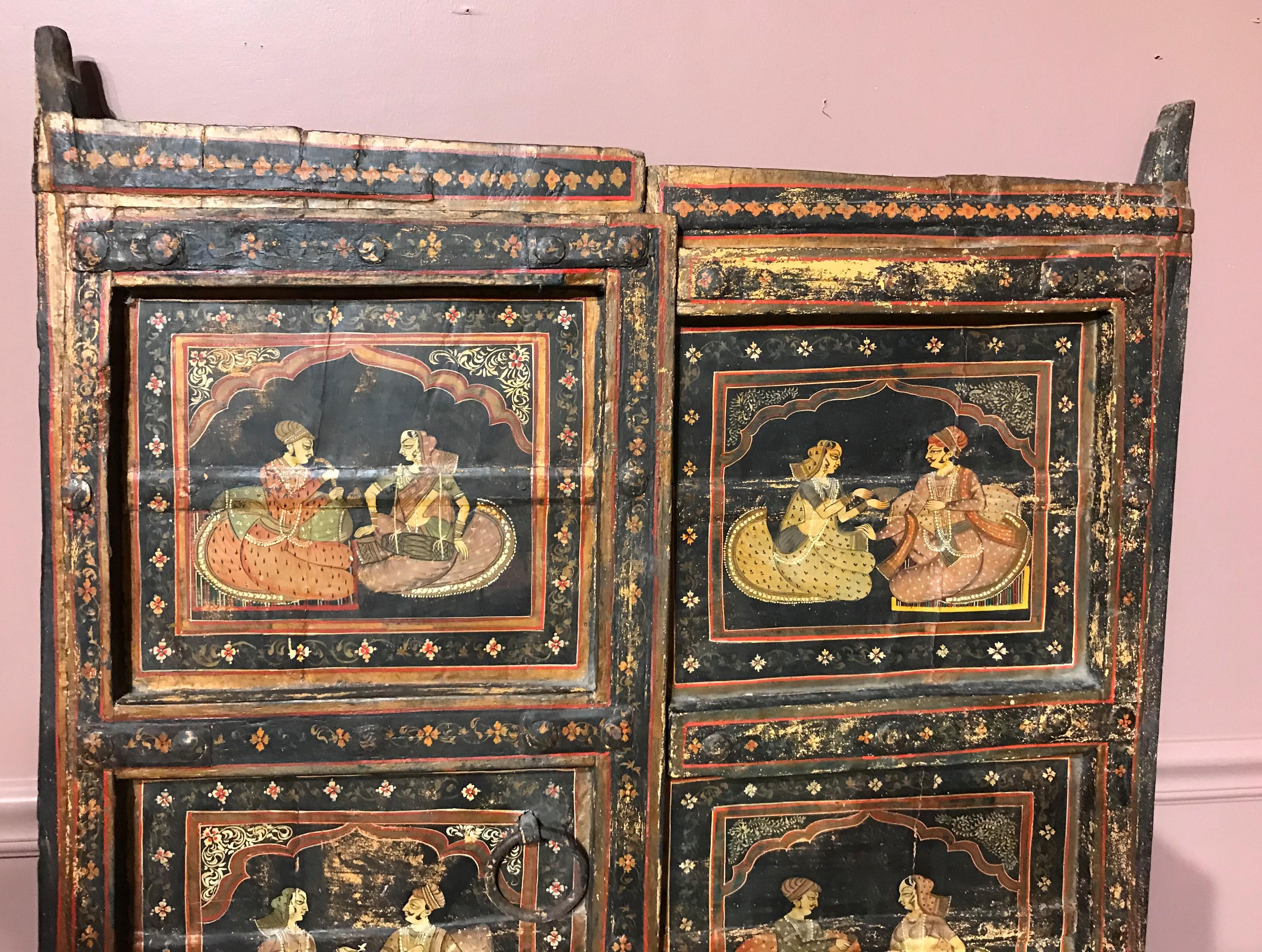A pair of heavy wooden polychrome doors, depicting genre scenes of a man and woman on each panel, surrounded by foliate decoration, with ebonized backs, and five supports slats on each door. The doors have retained some of their original iron