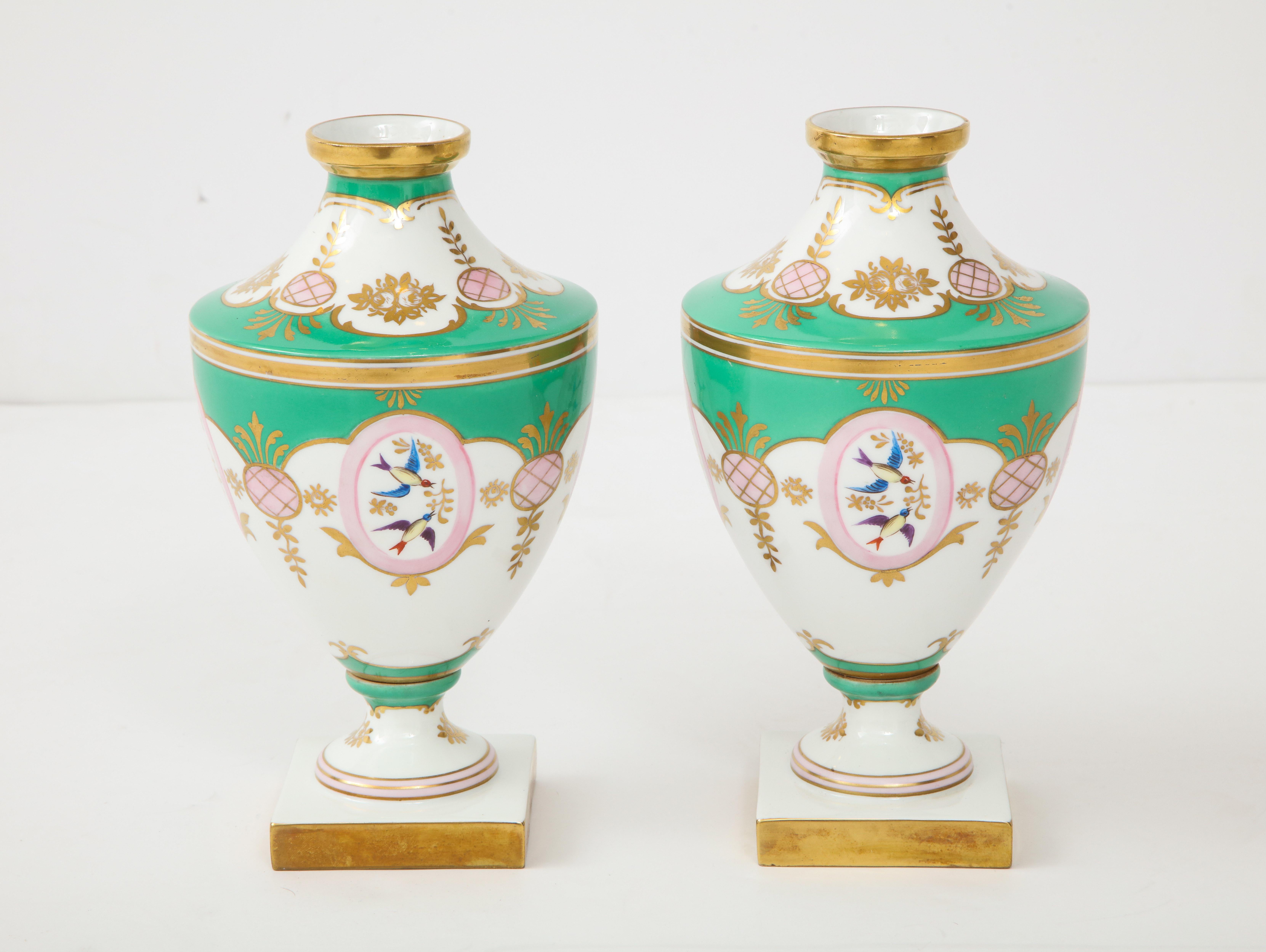Pair of exquisite 19th century hand decorated porcelain urn vases depicting blue birds in flight against white and pistachio green backgrounds, 22-karat gold trim.