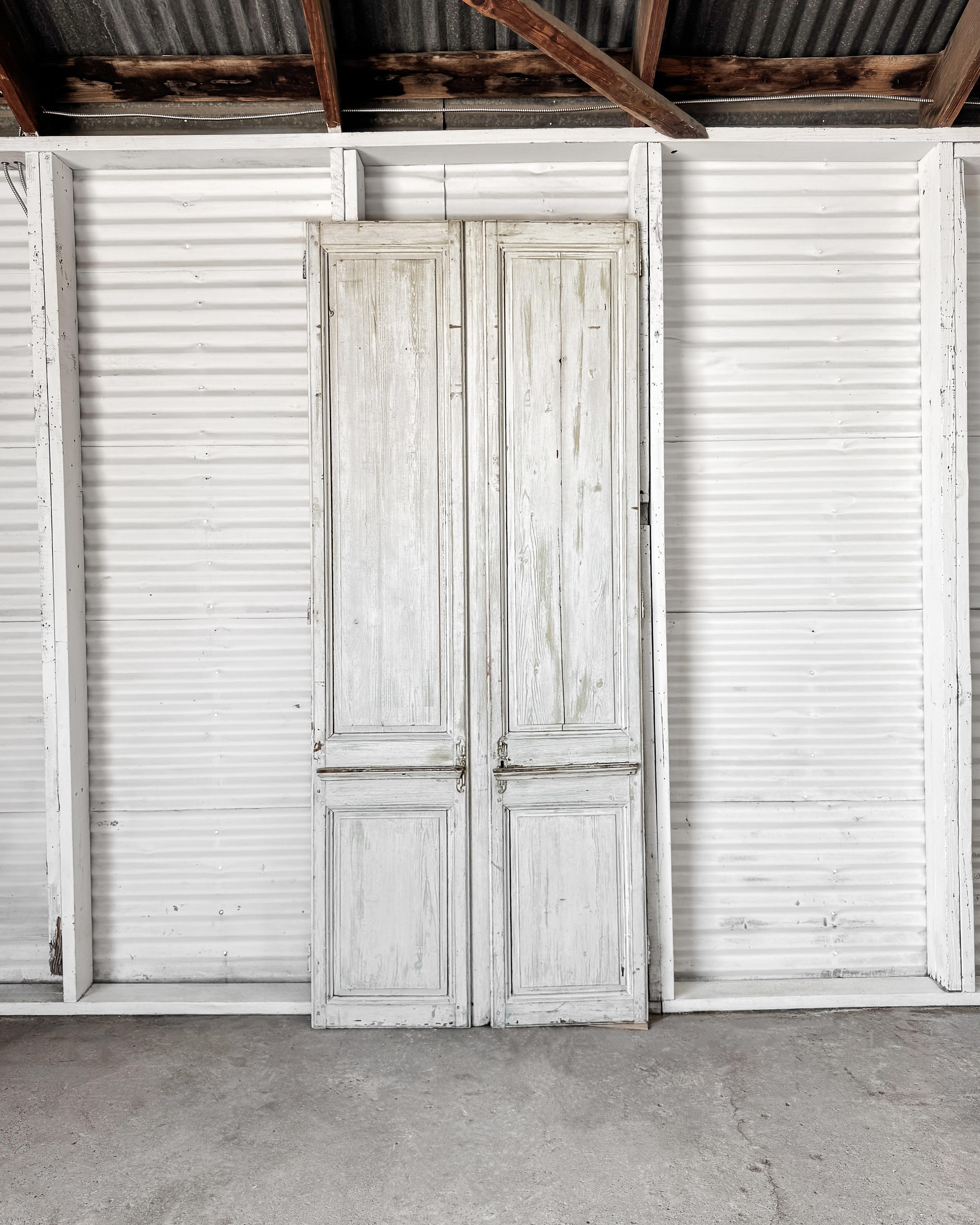 Desgastadas por el tiempo y suavizadas por capas de pintura blanca pálida y fría, este par de antiguas puertas francesas de abeto cuentan una tranquila historia de edad y autenticidad. El diseño de dos paneles es sencillo y simétrico, con un sutil