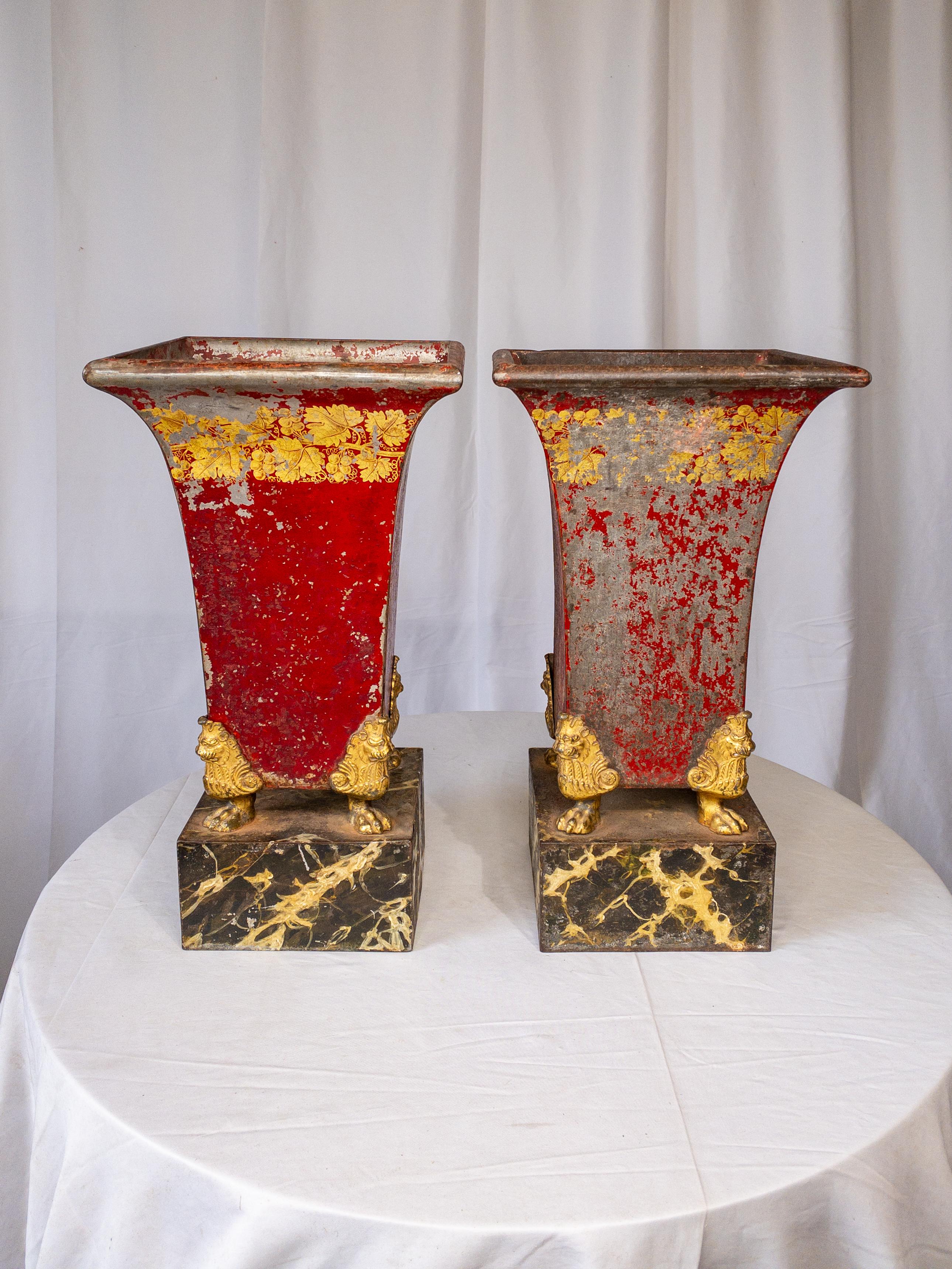 This pair of 19th-century red painted and gilt tole jardinieres on a faux marble stand exudes timeless elegance and charm. Crafted from tole painted metal, they boast intricate designs adorned with gilt bronze cupids, delicately perched on four gilt