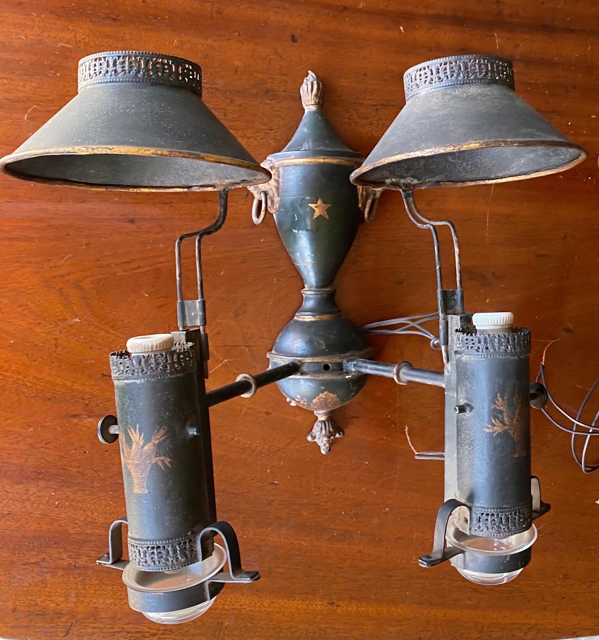 Great pair of 19th century Regency double light paint decorated tole sconces. Original oil vessels, removable shades with punchwork decoration, lions head pulls, and paint decoration throughout. 

Converted to electricity- just rewired and ready