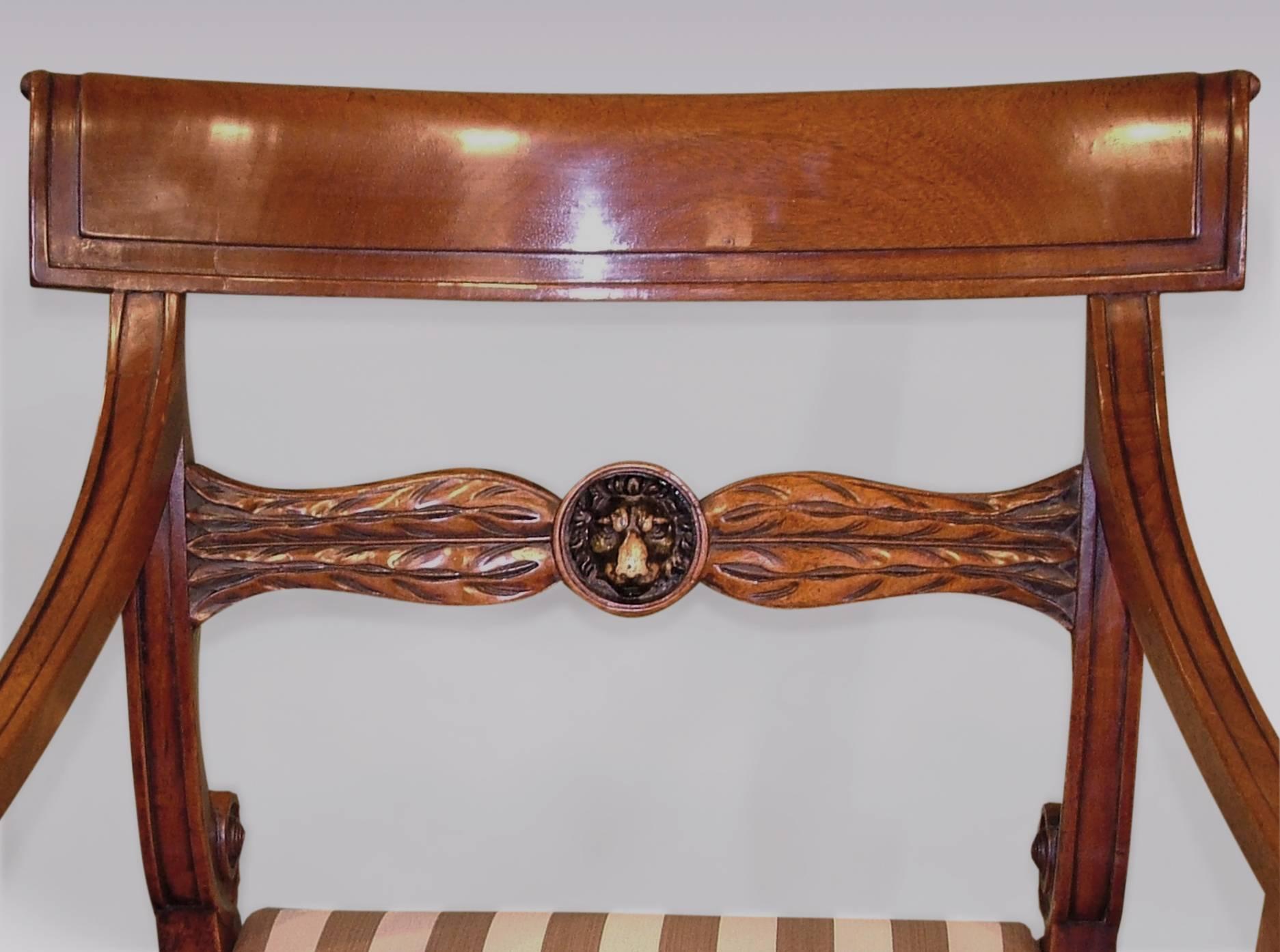 A matched pair of early 19th century Regency period mahogany armchairs, having paneled scroll over backs above leaf carved and lion's head crossrails. The armchairs having lion's paw arm supports raised on sabre legs.