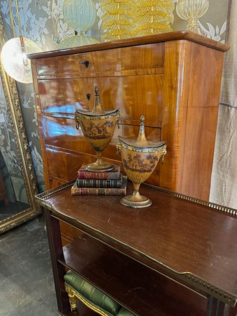 Coppia decorativa di urne dipinte in stile Regency con coperchio. Caratterizzato da una bella scena di paesaggio. Queste vere e proprie opere d'arte sarebbero un accessorio favoloso. Circa 1920.
13h x 7w x 5d
